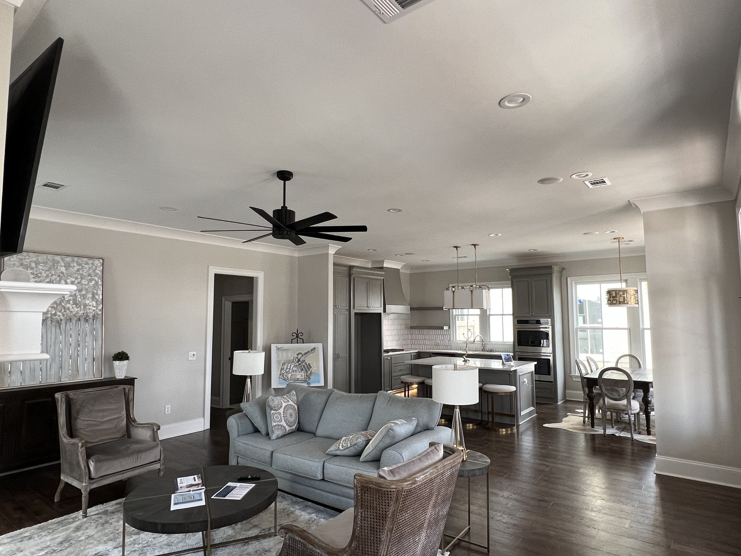 Open-concept living room and kitchen with gray cabinets, white walls, hardwood floors, and large windows, including seating area with a sofa, armchair, and coffee table.