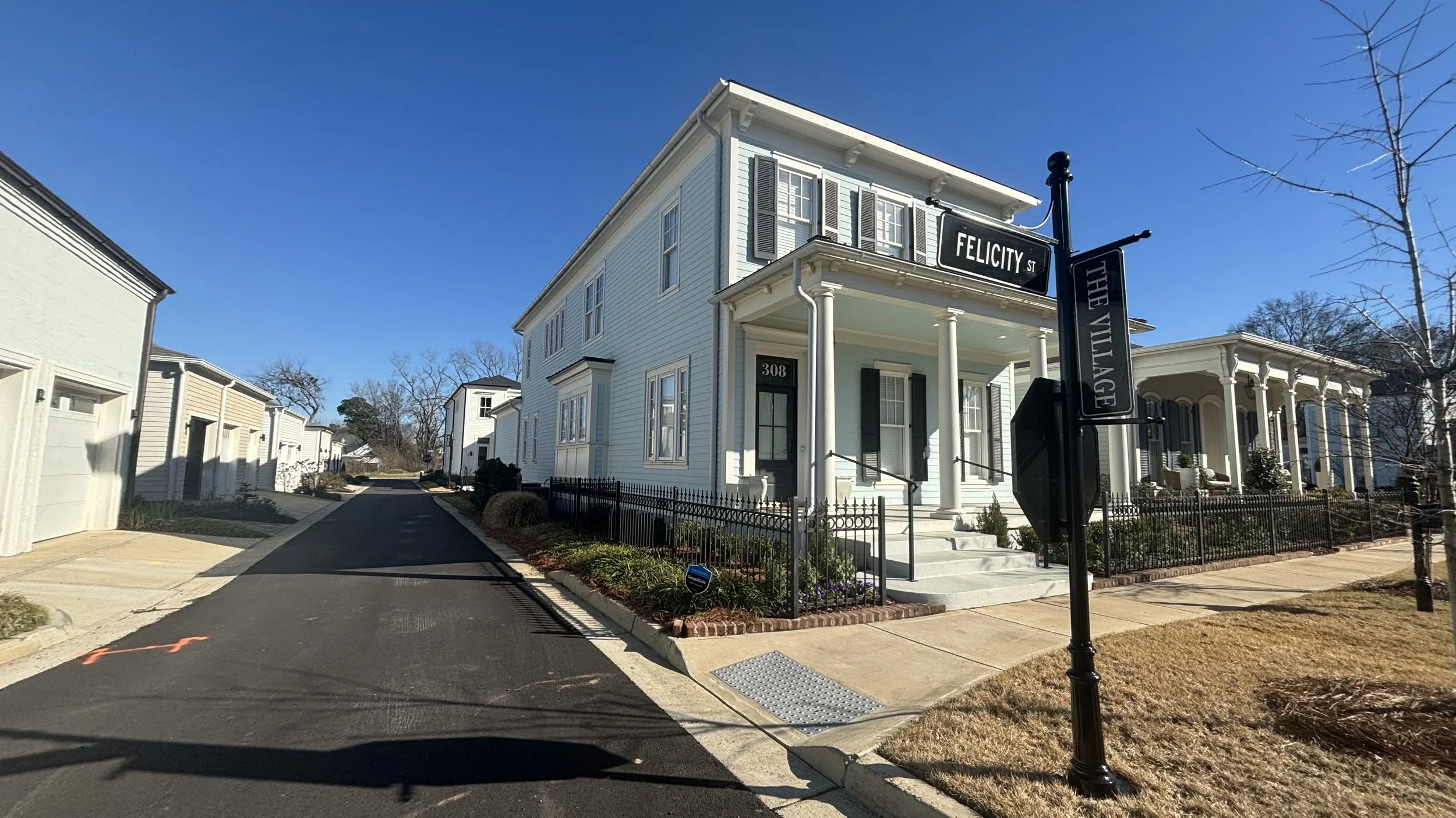 White historic-style house with black shutters on Felicity Street, with a sign reading "The Village" hanging on the lamp post outside.