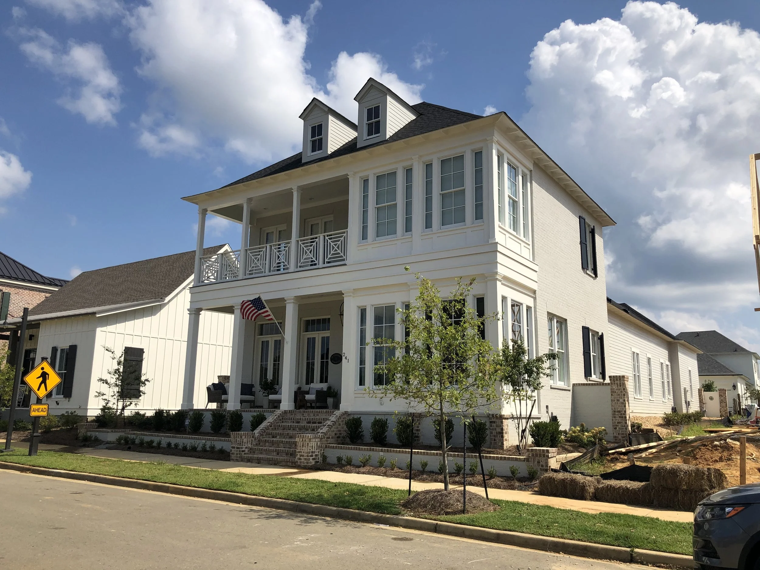 A large white multi-story house with a front porch, multiple windows, and decorative black shutters, under a partly cloudy sky.