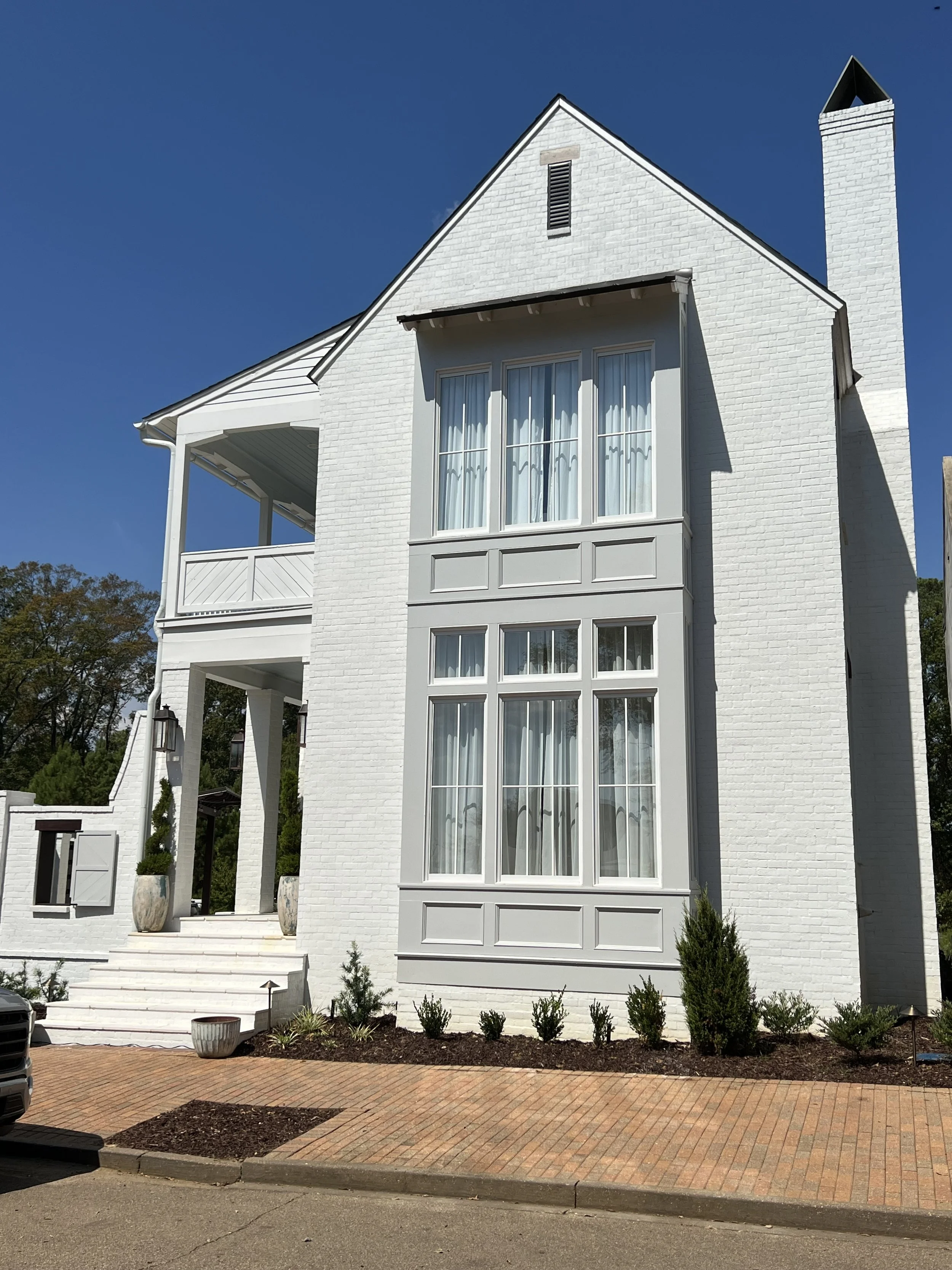 White multi-story house with large windows and a balcony, set against a clear blue sky.
