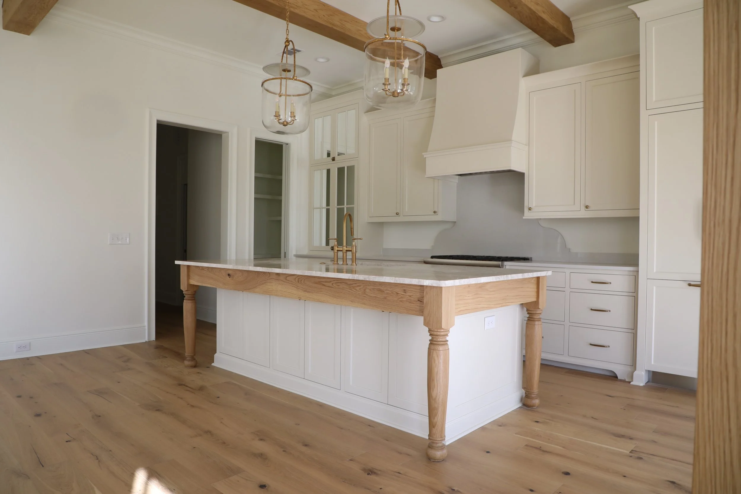 Modern kitchen with white cabinets, a center island with a marble top, a gold faucet, and wooden beams on the ceiling.