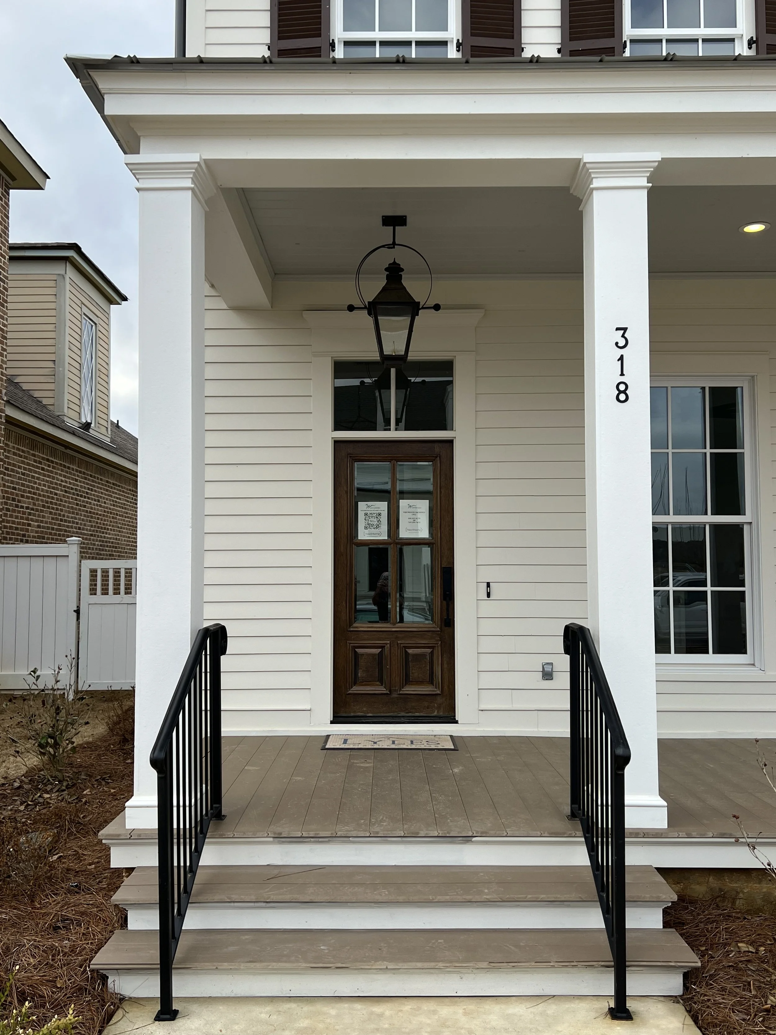 Front porch of a house with a wooden door, black railing stairs, white columns, and a black lantern hanging from the ceiling.