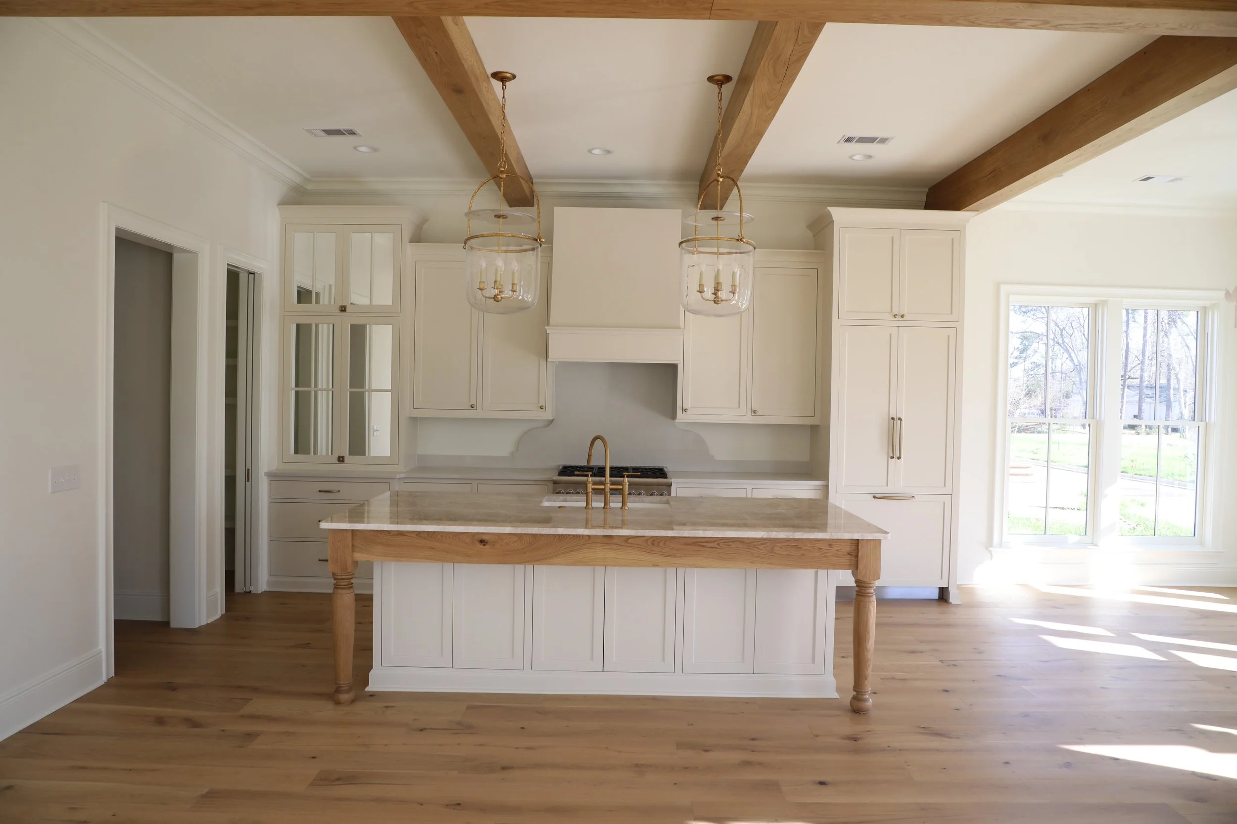 Bright, modern kitchen with white cabinetry, a wooden island with a marble countertop, and large windows allowing natural light. Pendant lights hang above the island.