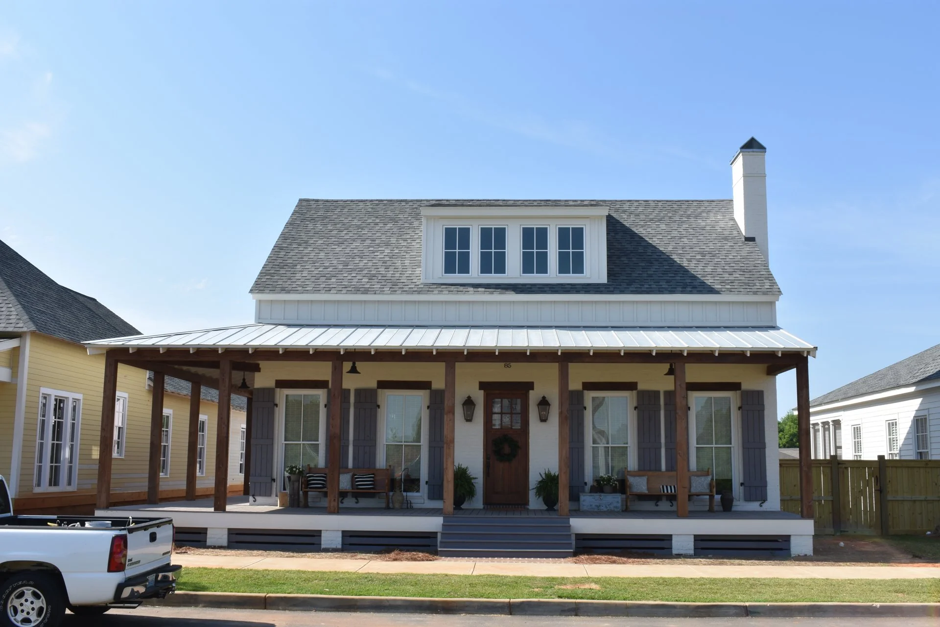 Front view of a modern two-story house with a porch, gray shutters, a wreath on the front door, and a chimney, under a blue sky