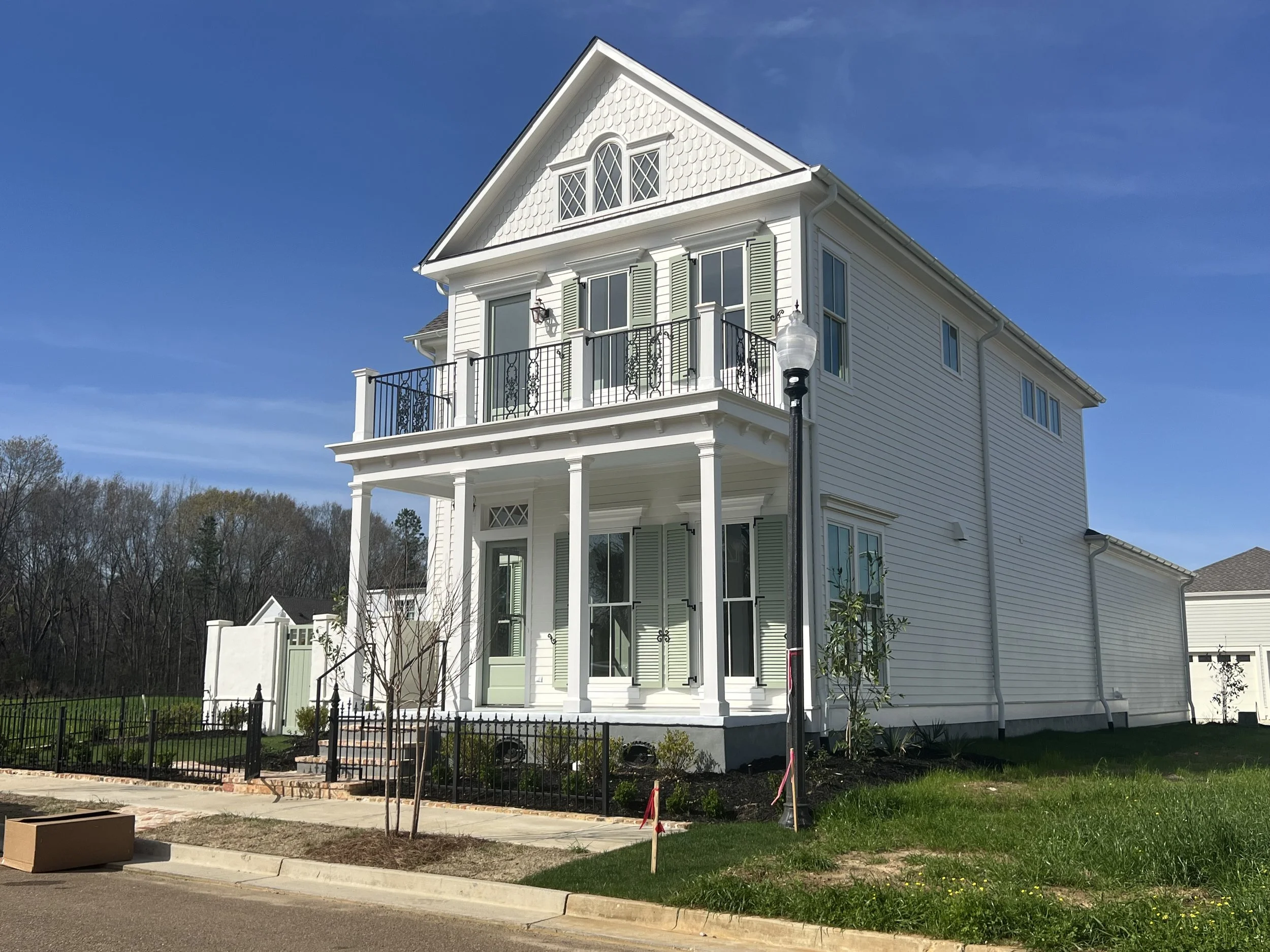 A large white three-story house with a front porch, balcony, and multiple windows, under a clear blue sky.