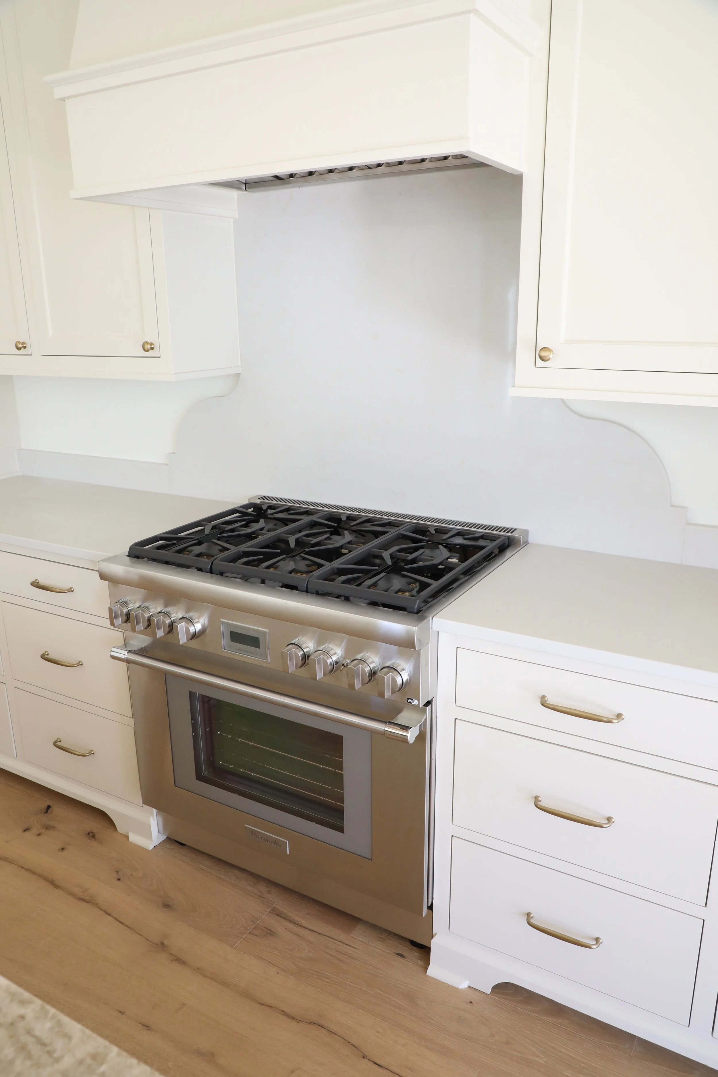 White kitchen with a stainless steel oven and stovetop, white cabinets, and hardwood floor.