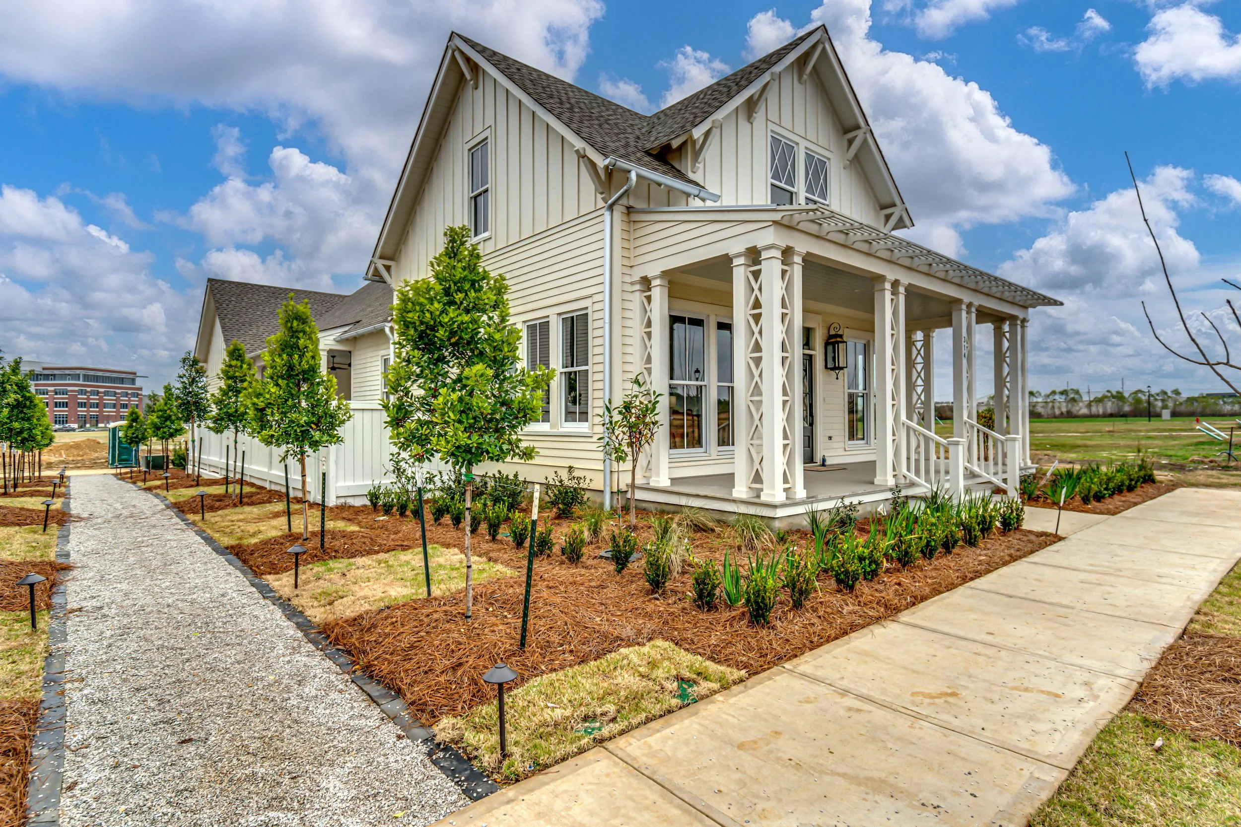 Newly built white house with a porch, surrounded by young trees, and pathways in a grassy area.