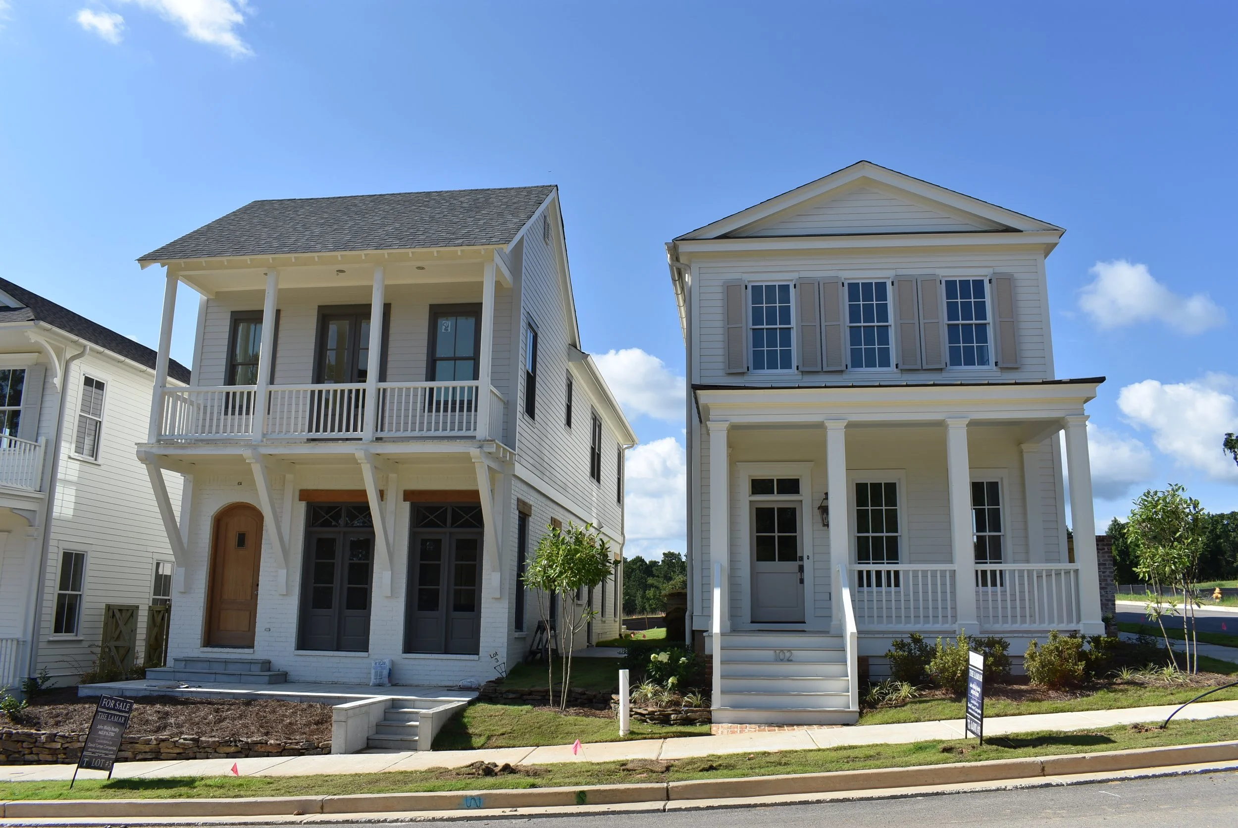 Two modern white houses with front porches and stairs, under a blue sky with clouds.