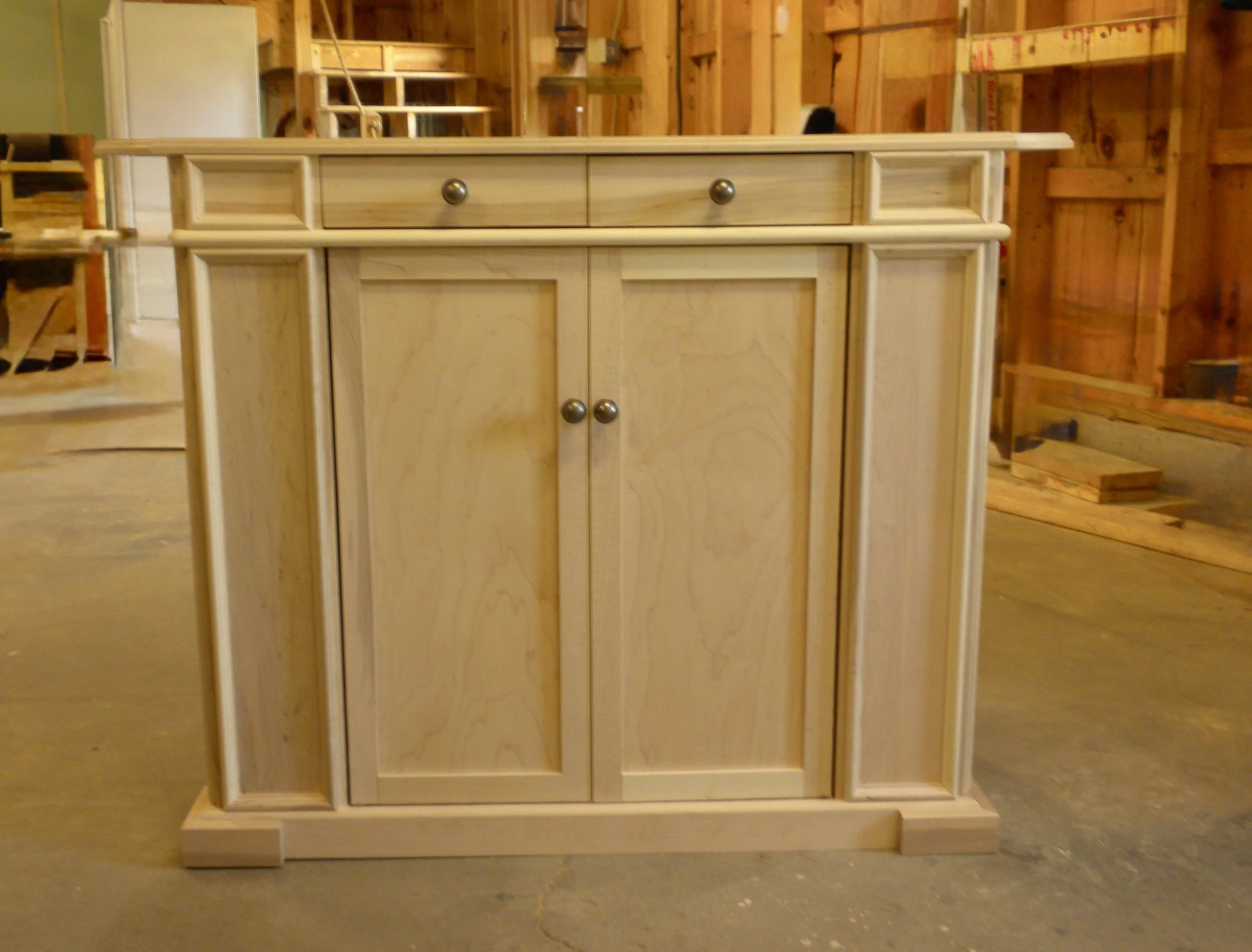 unfinished wooden cabinet with two doors and three drawers in a woodworking shop.