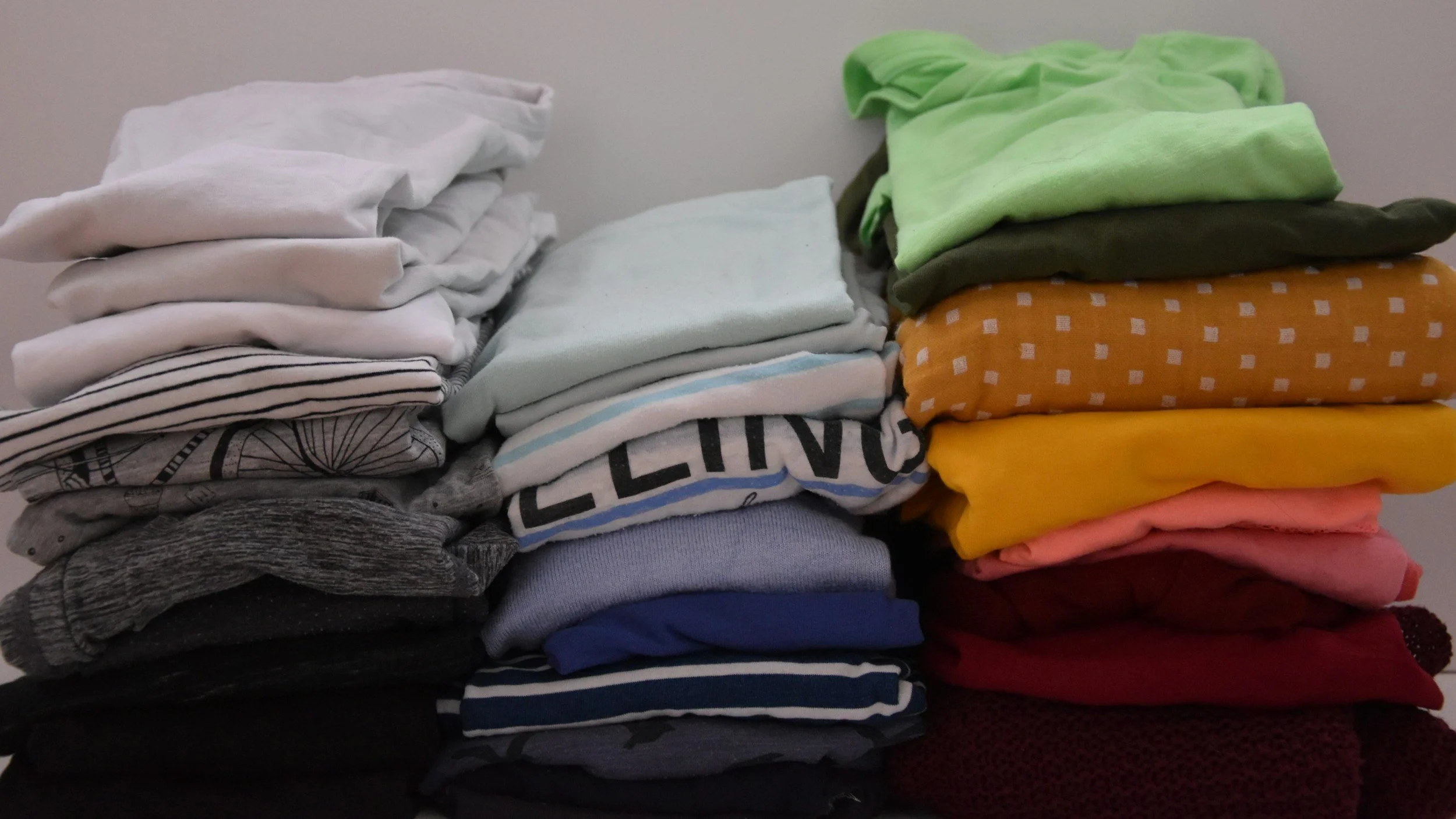 Piles of folded clothes including t-shirts, pants, and sweatshirts in various colors and patterns.