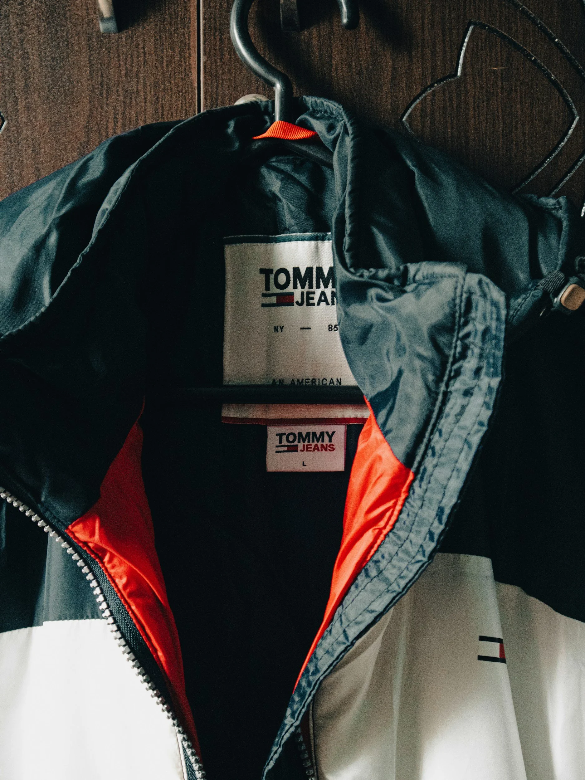 Tommy Jeans black and white jacket with red interior lining hanging on a wooden surface.