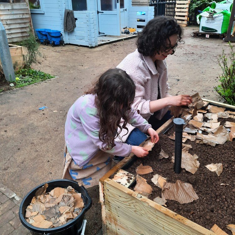 Two children working on a garden project, placing decorative stones in a bordered flower bed.