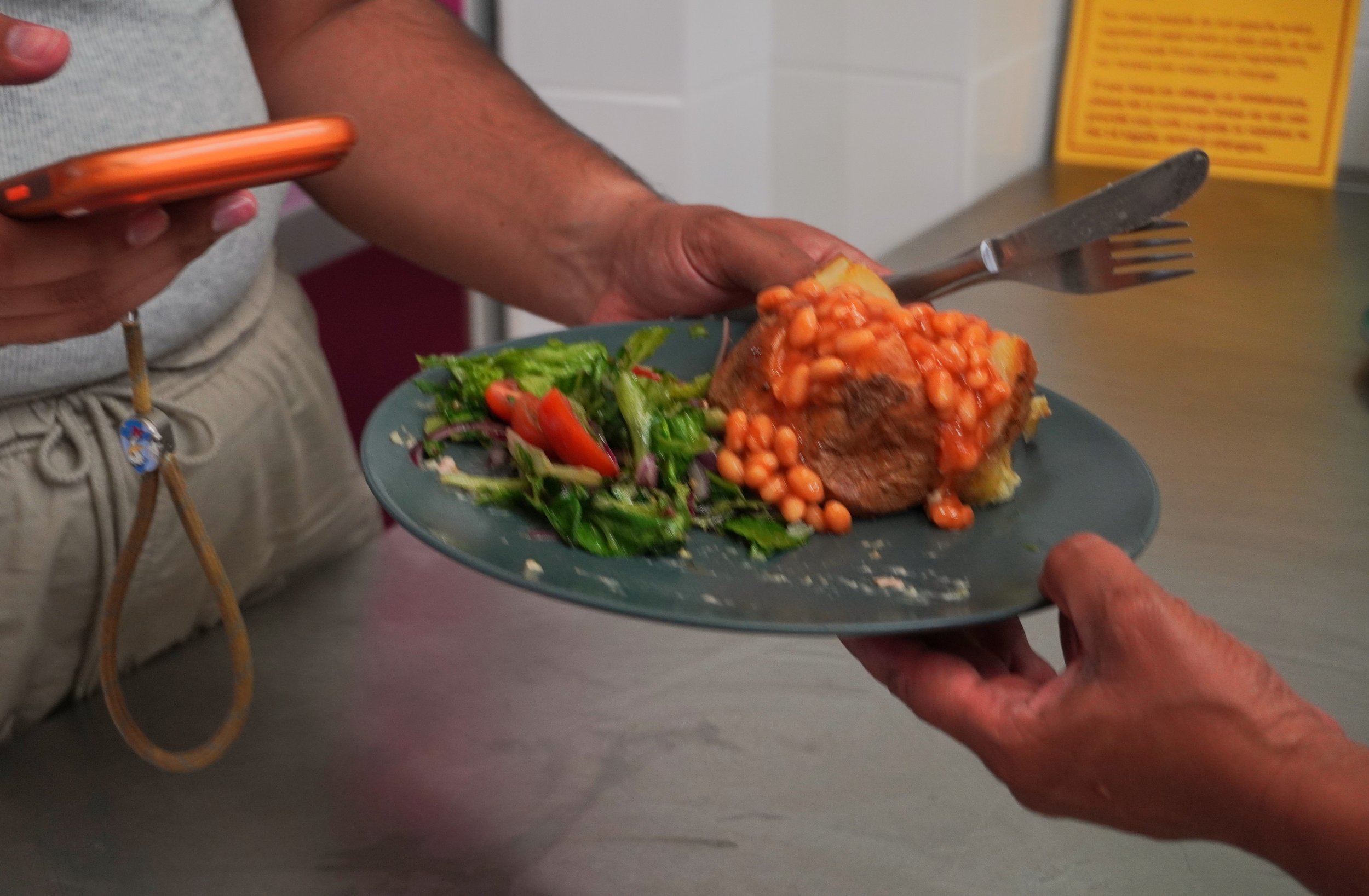 One hand holds out a plate of food for another to hold. This person is also holding a fork and knife