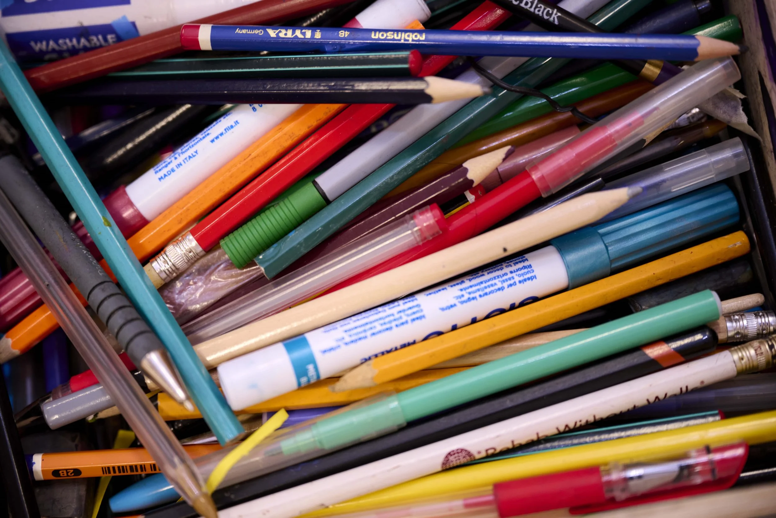 A collection of colored pencils, pens, and markers inside a container.