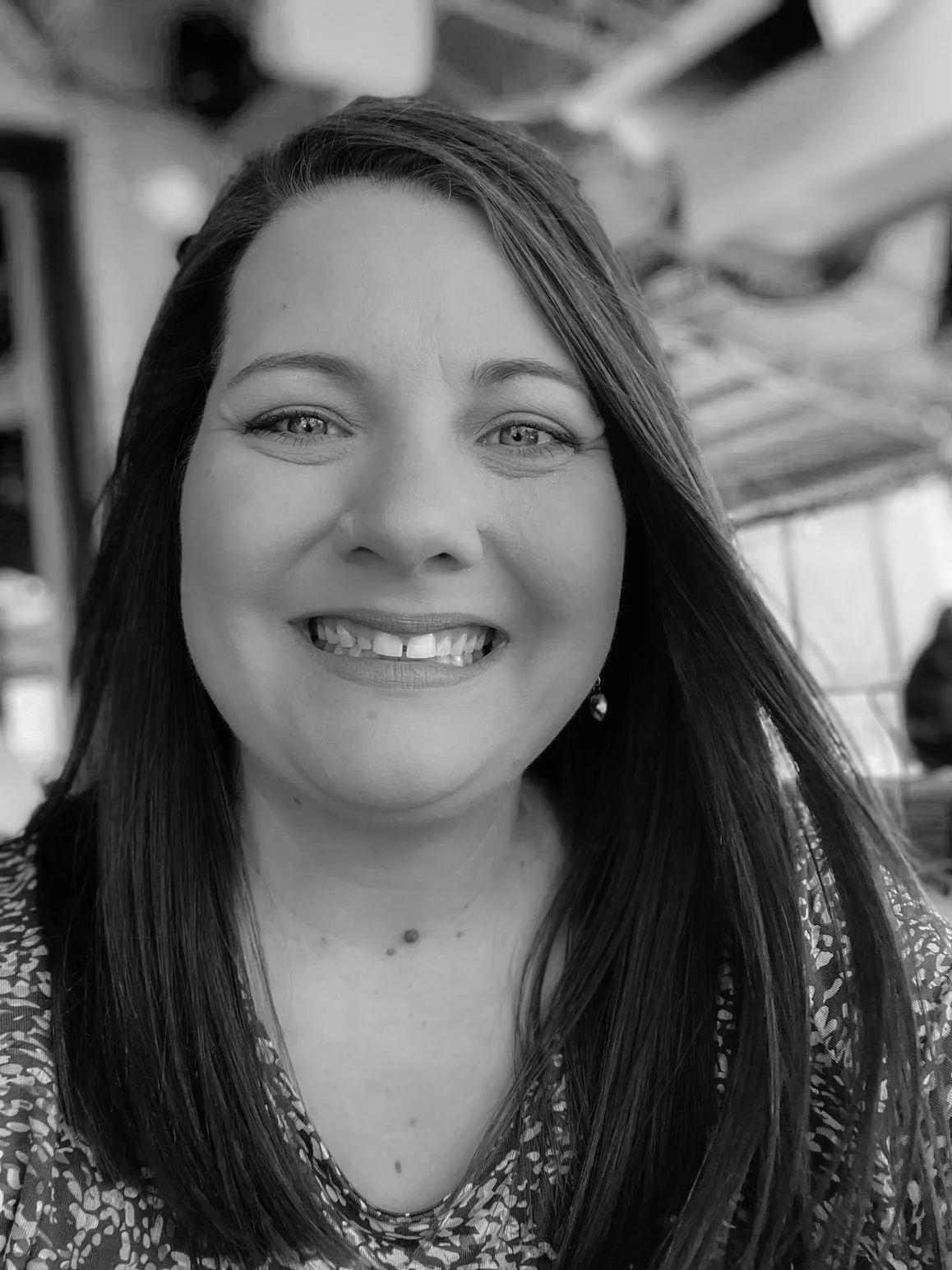 A smiling woman with long dark hair, wearing a patterned top, in an indoor setting.