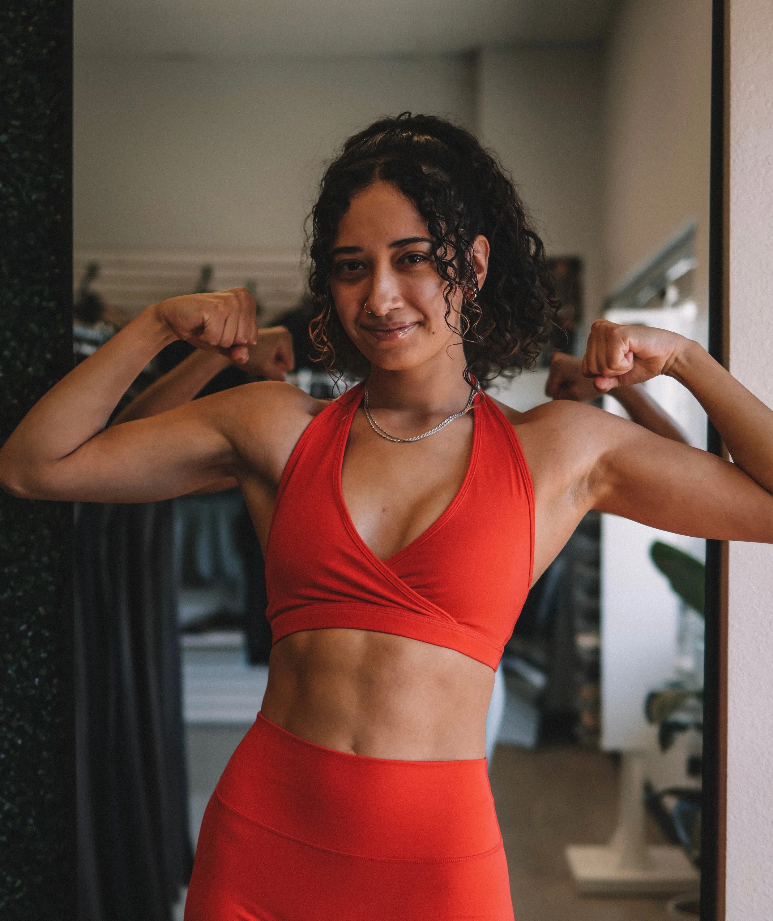 Young man with dark hair and beard wearing a white t-shirt standing against a light-colored wall.