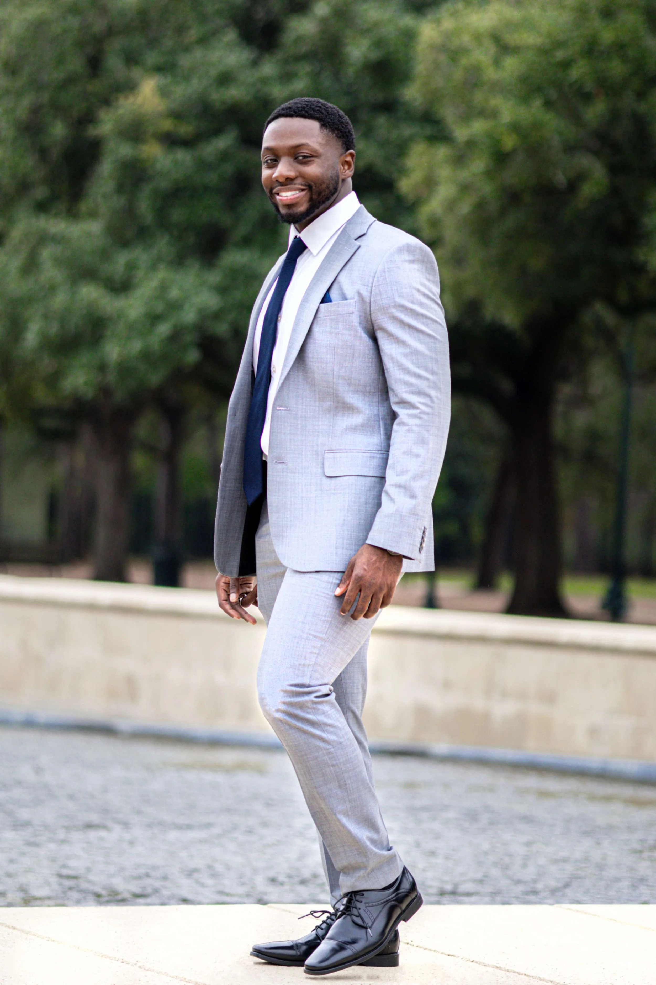 A young woman with black hair tied in a messy ponytail, wearing a denim jacket and hoop earrings, looking into the camera against a light pink background.