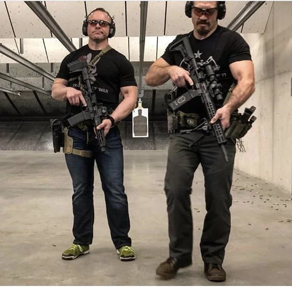 Two men holding rifles and wearing safety glasses and headphones at a target shooting range.