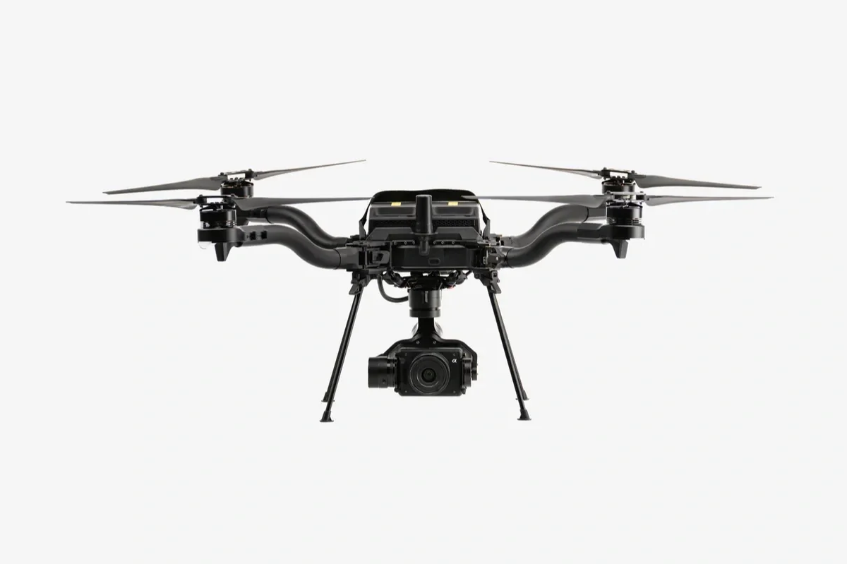 A black quadcopter drone with a camera mounted underneath, set against a plain white background.