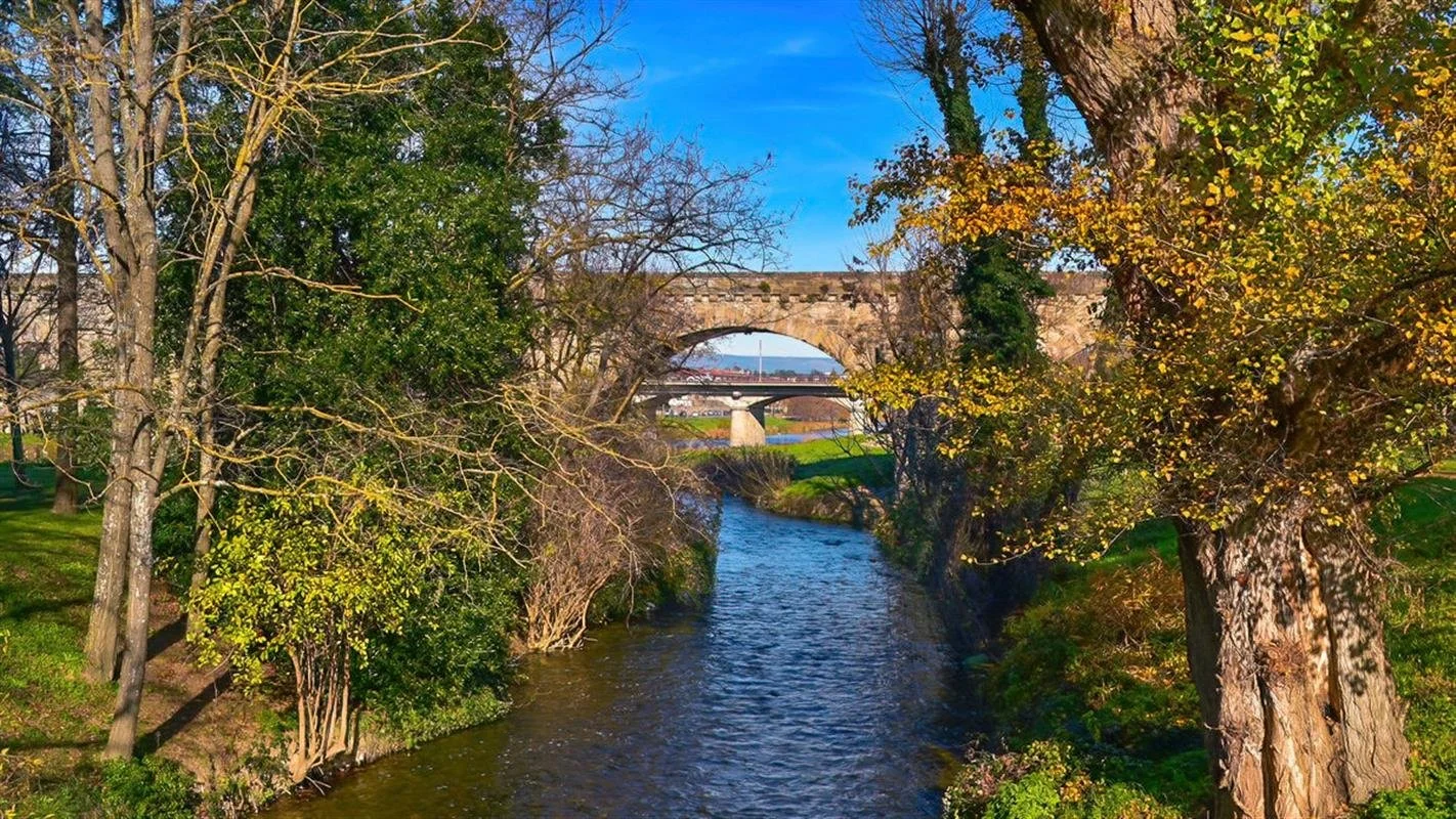 A small river with trees on both sides, an old stone bridge in the background, and a clear blue sky.