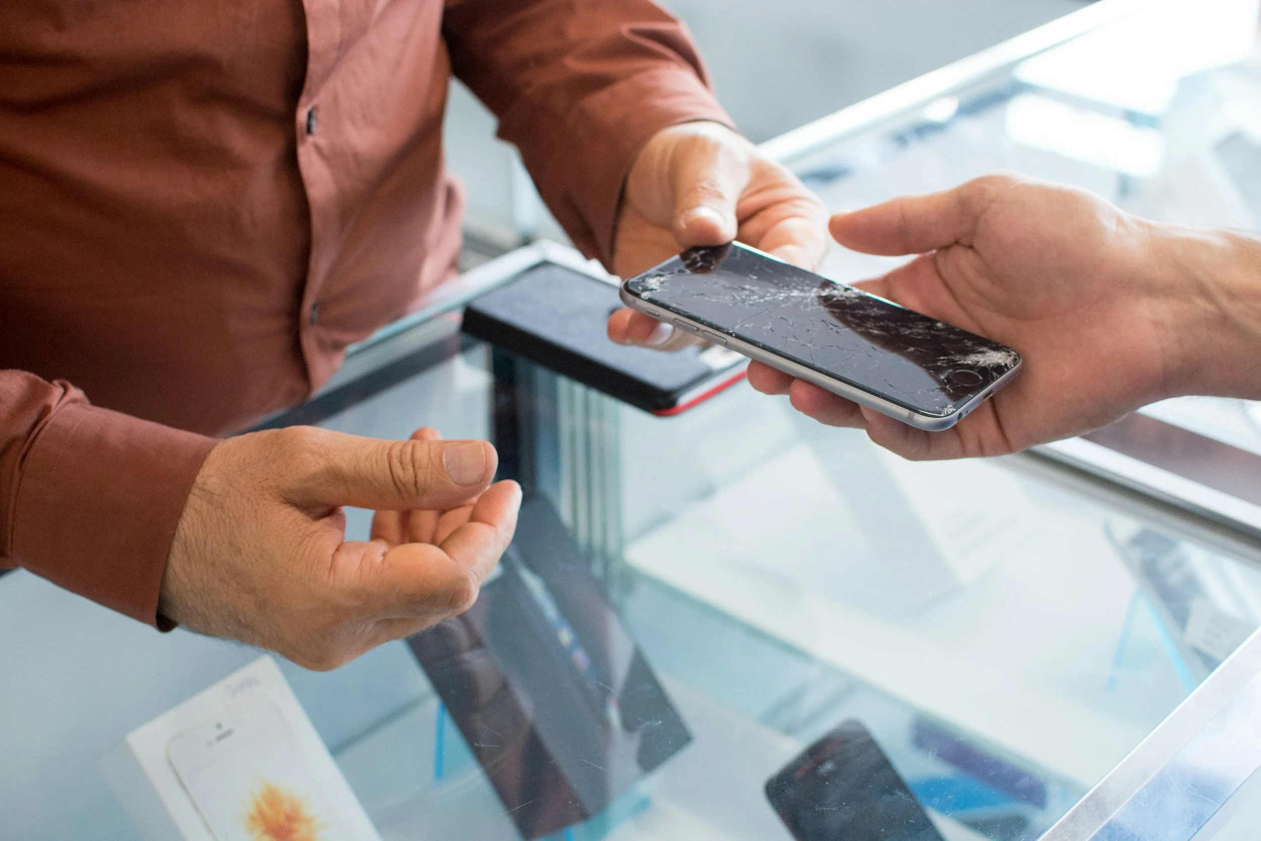Person handing a broken smartphone to another person in a store.