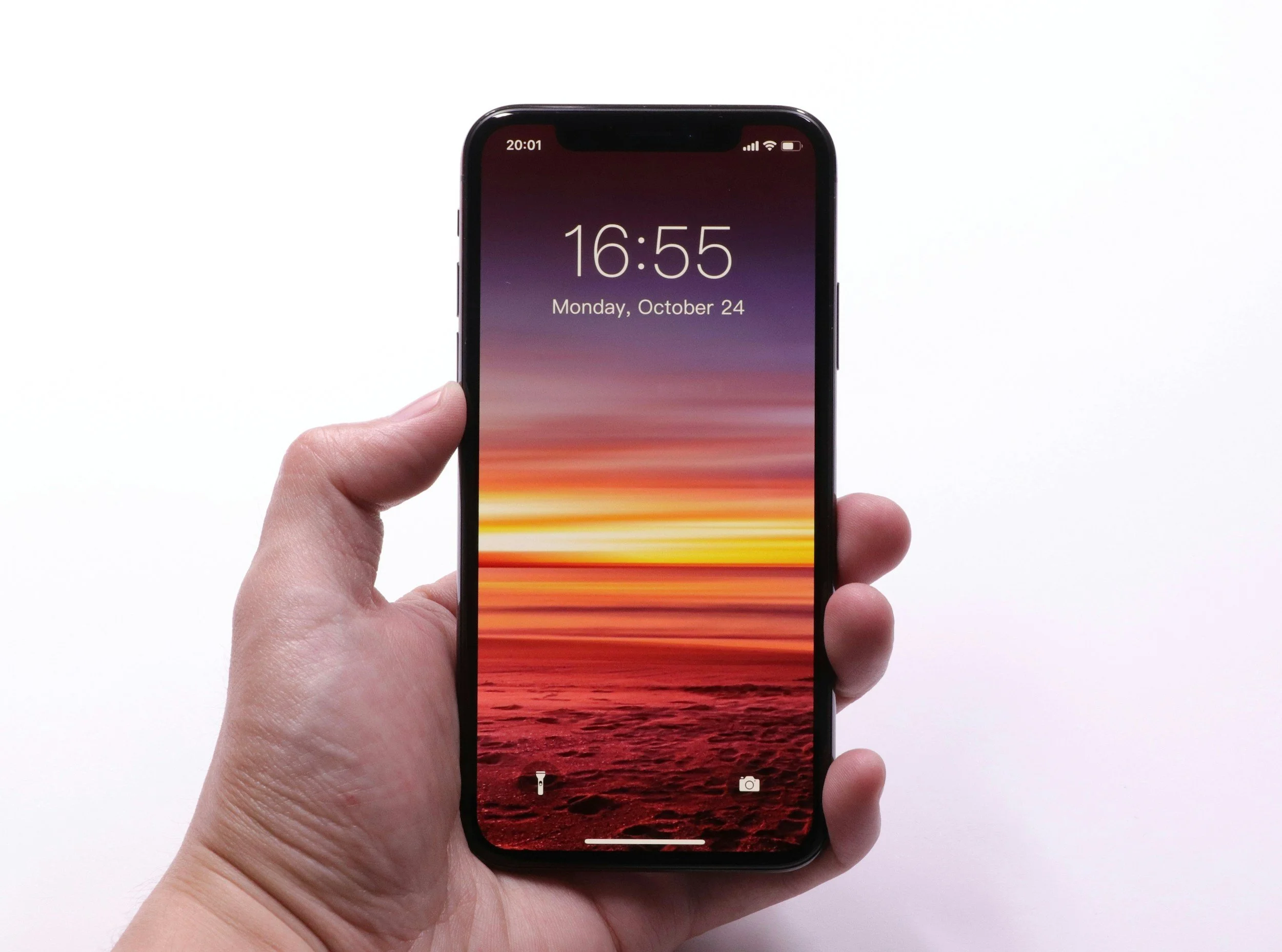 Hand holding a smartphone with a sunset or sunrise landscape wallpaper and the time 16:55 on the screen.