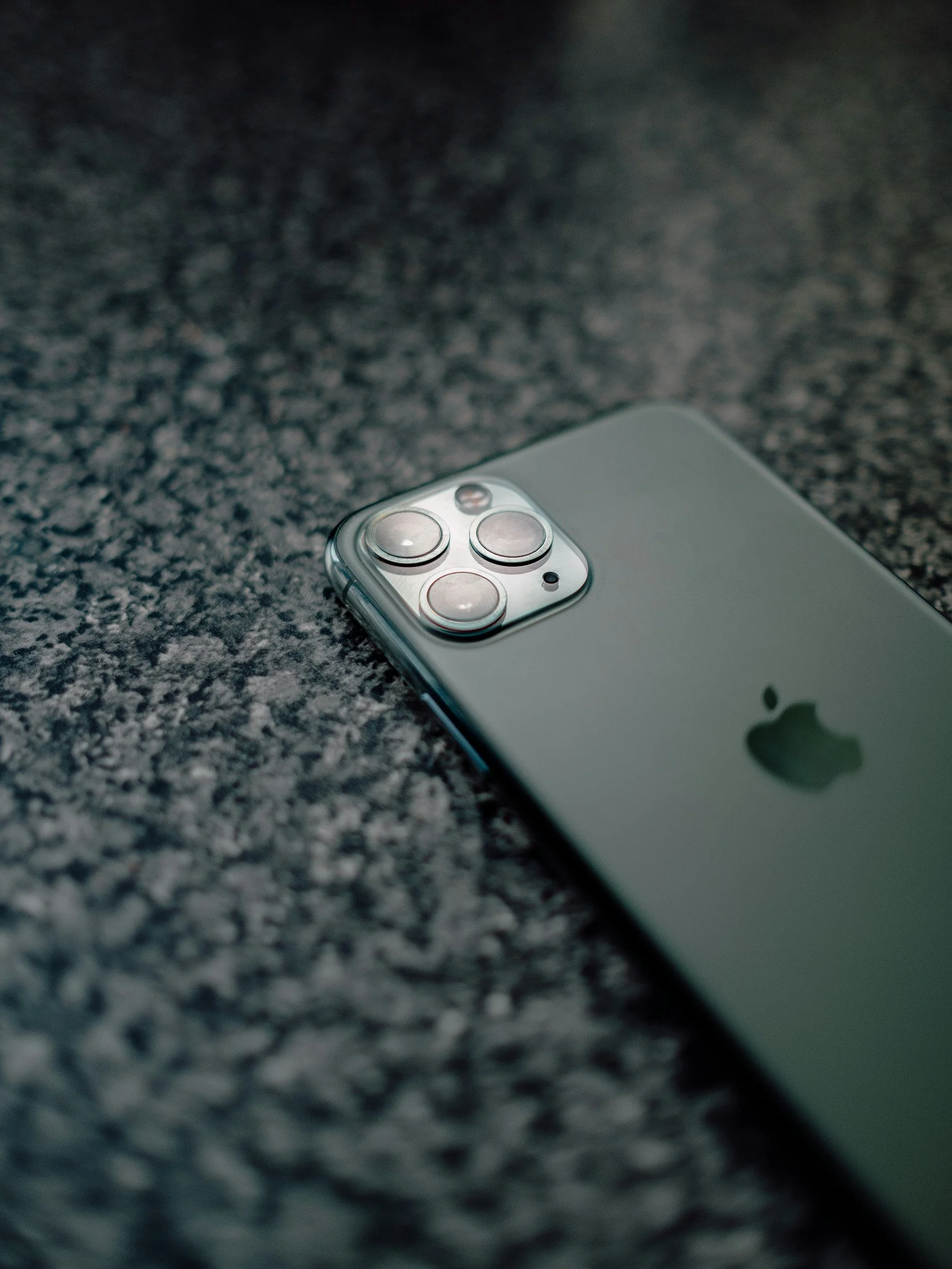 Close-up of a silver iPhone with triple camera setup lying on a textured dark surface.