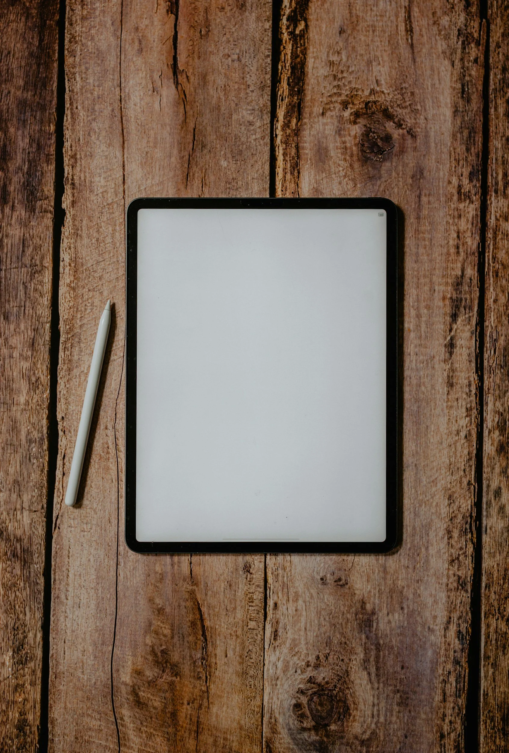 A tablet with a stylus placed on a rustic wooden surface.