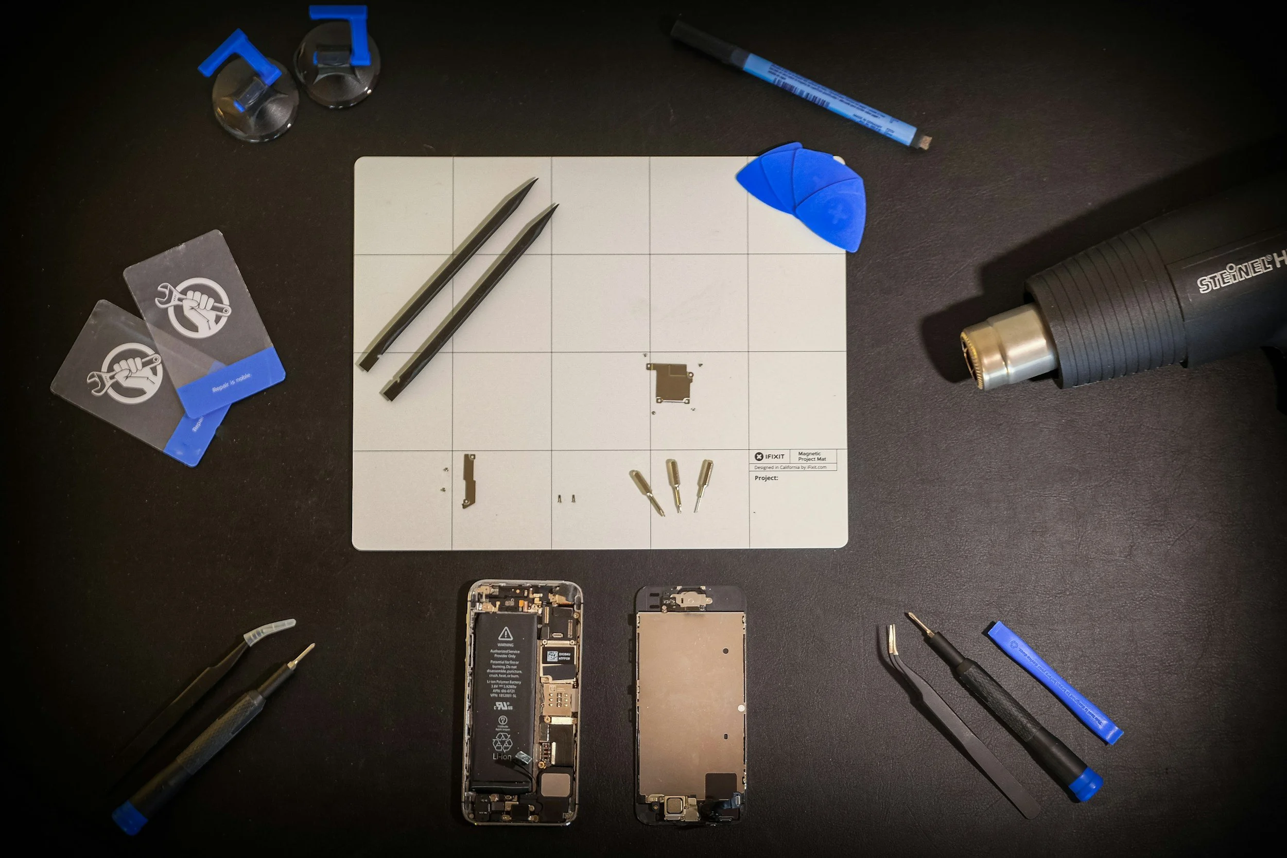 Disassembled smartphone, repair tools, and a work mat on a black surface.