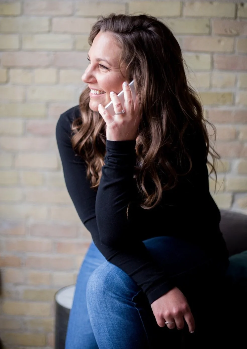 Alicia, founder of Boulevard North, Web and Creative, with long, wavy brown hair smiling and talking on a mobile phone with a website cliet, sitting against a brick wall, talking about their website project.