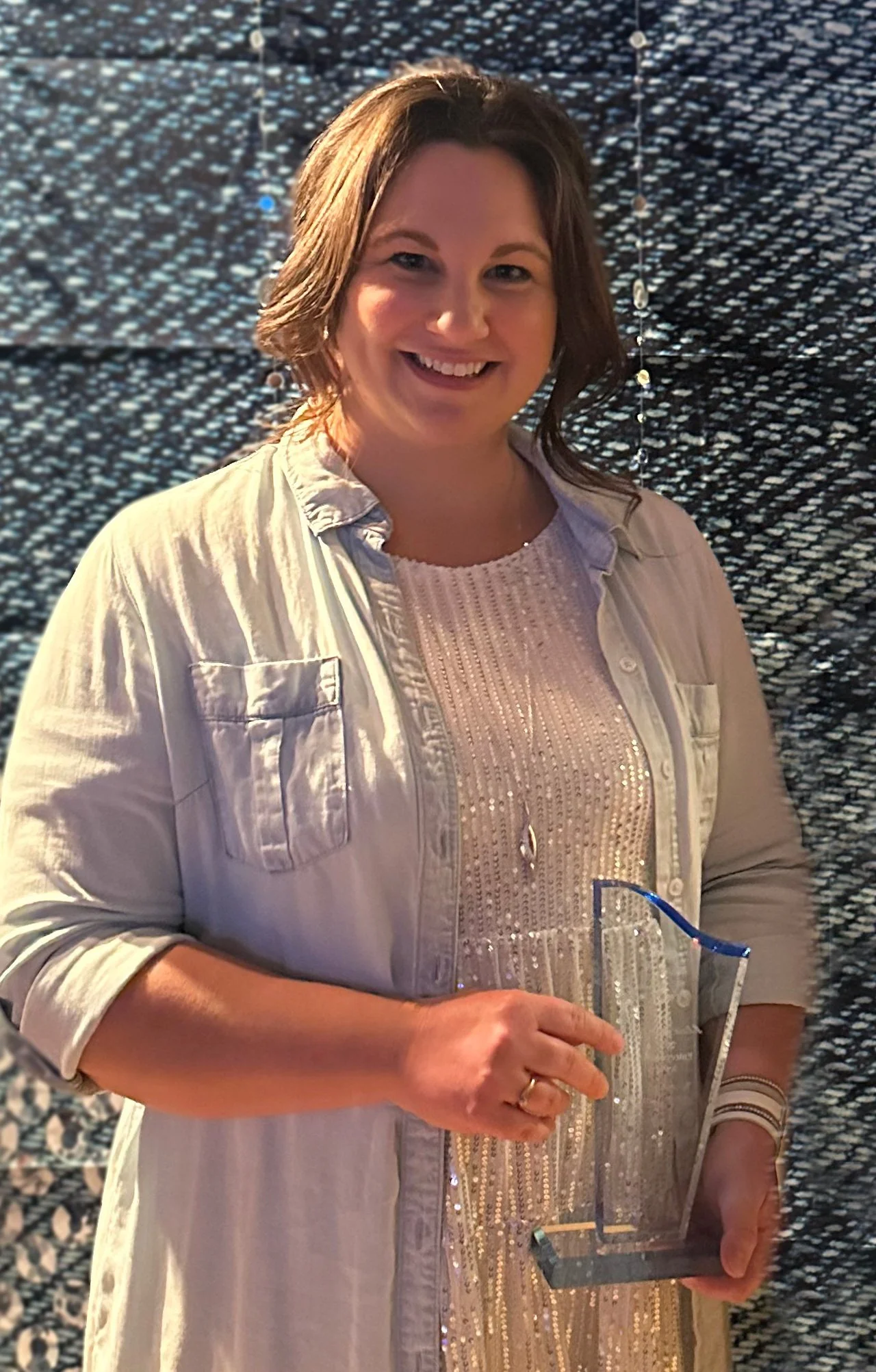 Alicia, founder of Boulevard North, Web and Creative, smiling, holding an award - Female Entrepreneur Award, dressed in a sparkly top and light-coloured button-up shirt, standing against a textured, dark background.