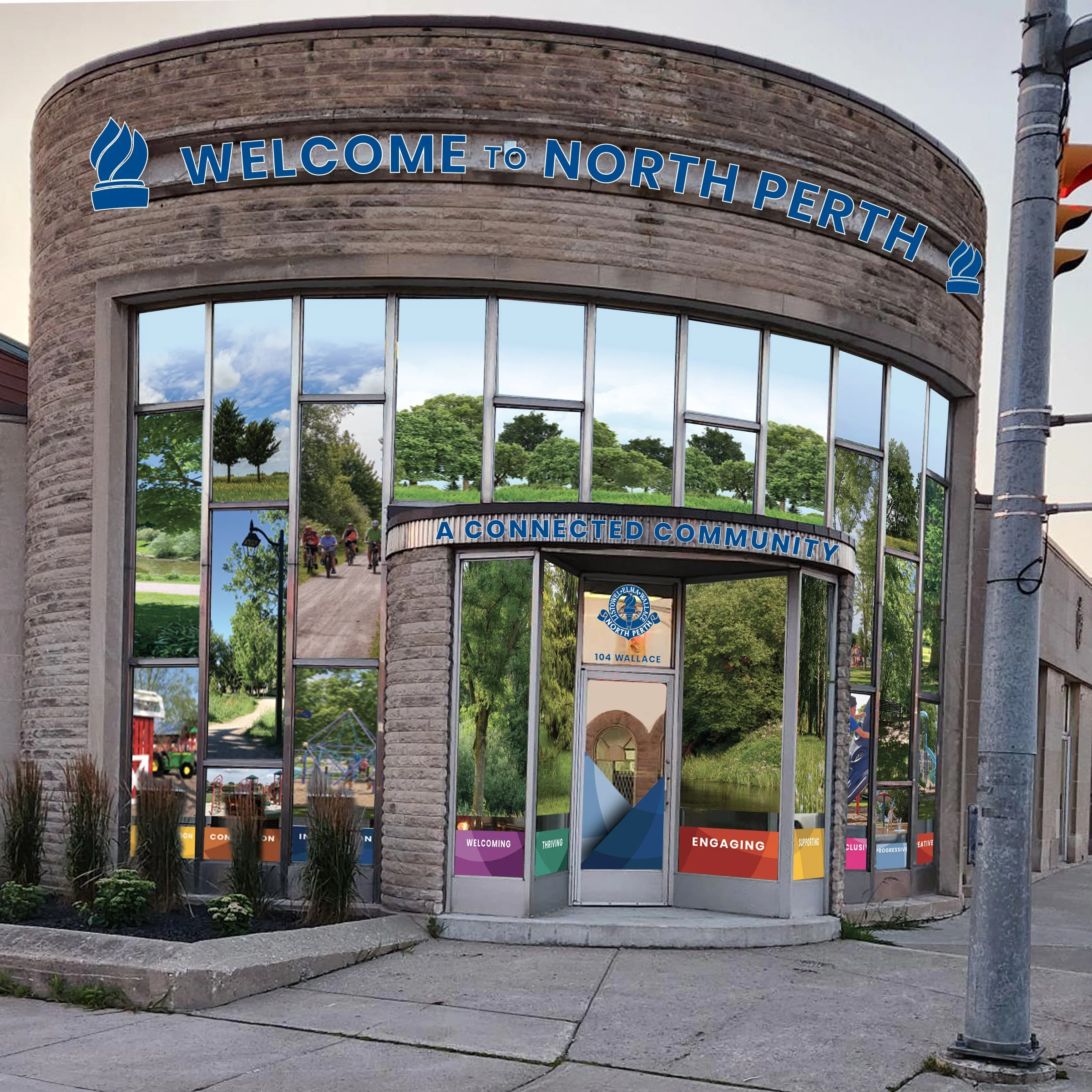 Building with large glass windows displaying surrounding trees and park area, with a sign above the door reading "A Connected Community" and an additional sign indicating the address as 104 Wallace. The building has a curved brick facade and a welcoming message with words like "Welcoming," "Thriving," "Engaging," and "Inclusive" at the bottom of the windows.