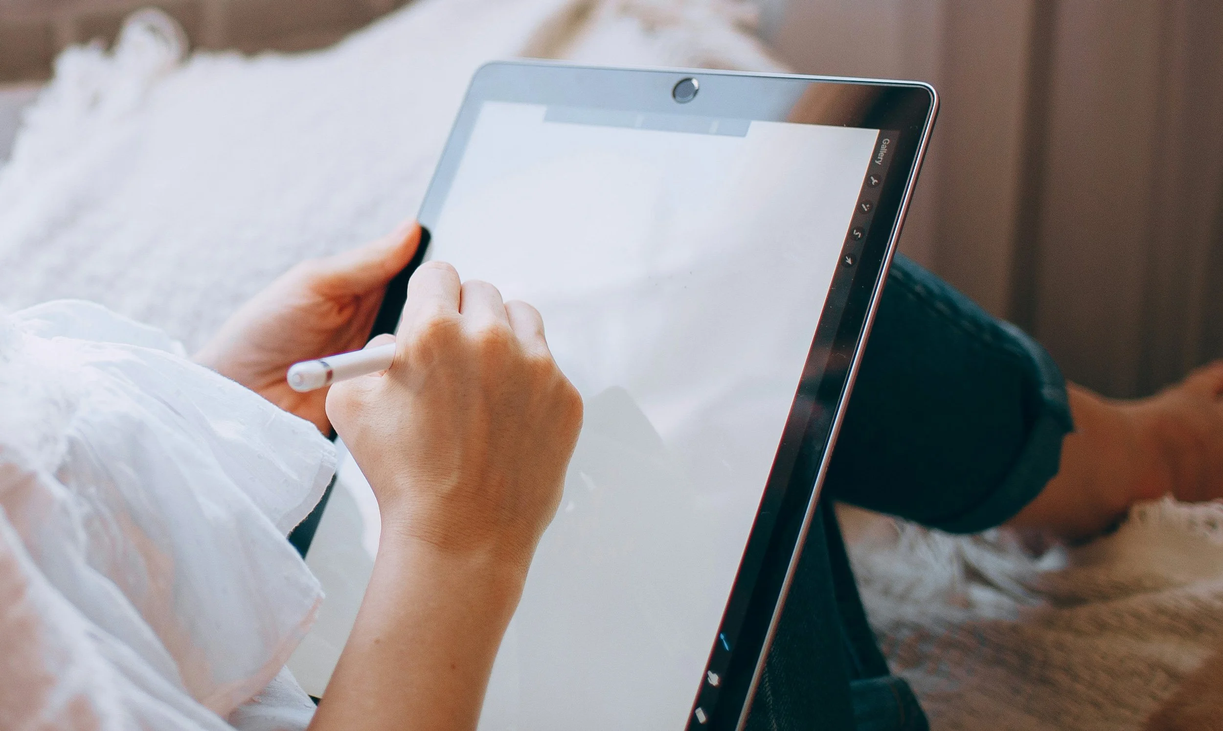Person holding a stylus and using a digital tablet, sitting with legs crossed on a comfortable surface. Planning the logo and branding project for a client. Professional design services on a budget.