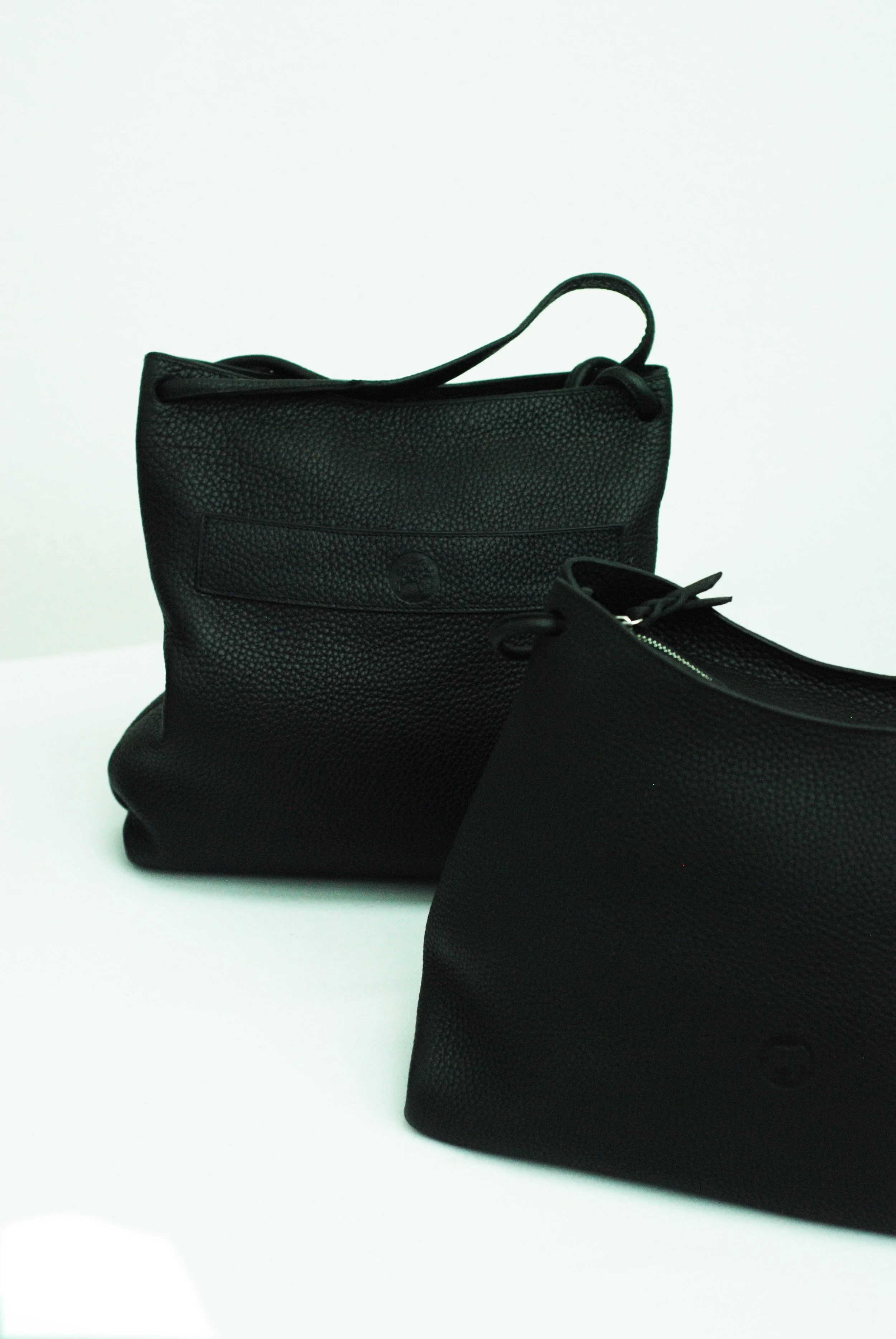 Two black textured leather bags placed on a white surface against a white background.