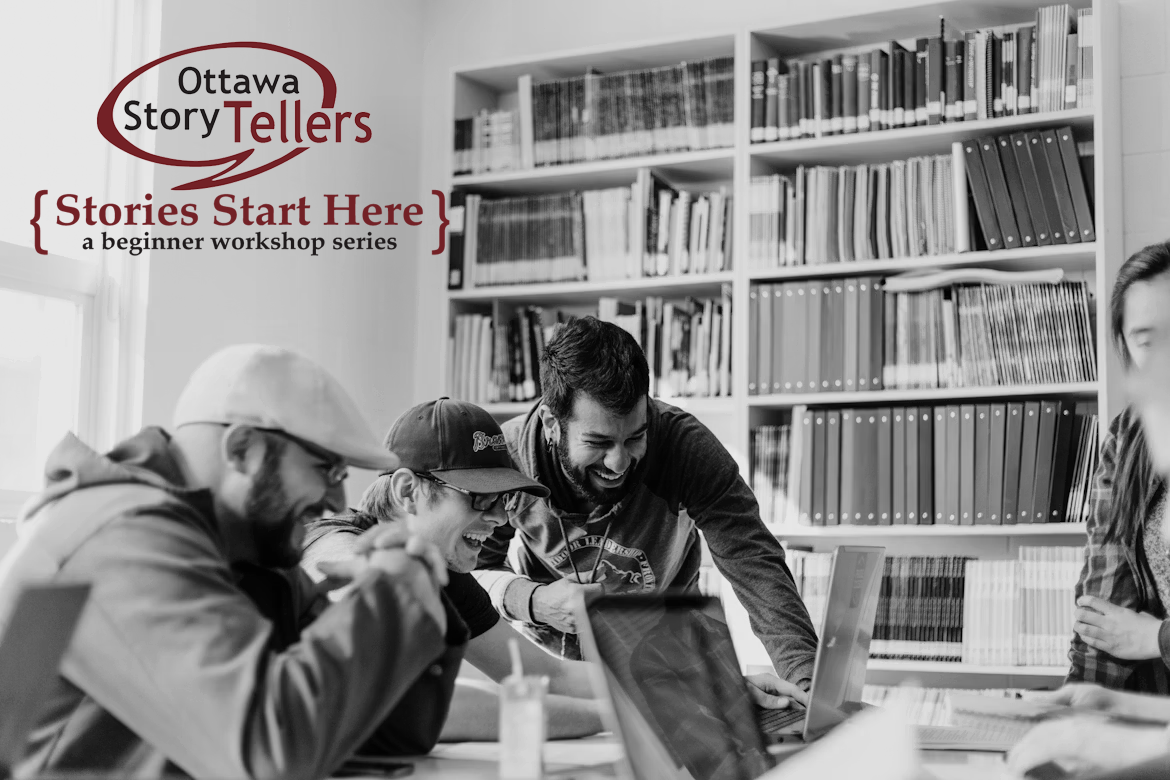 Four young men laughing and working together at a table in a library or study room, with bookshelves in the background.