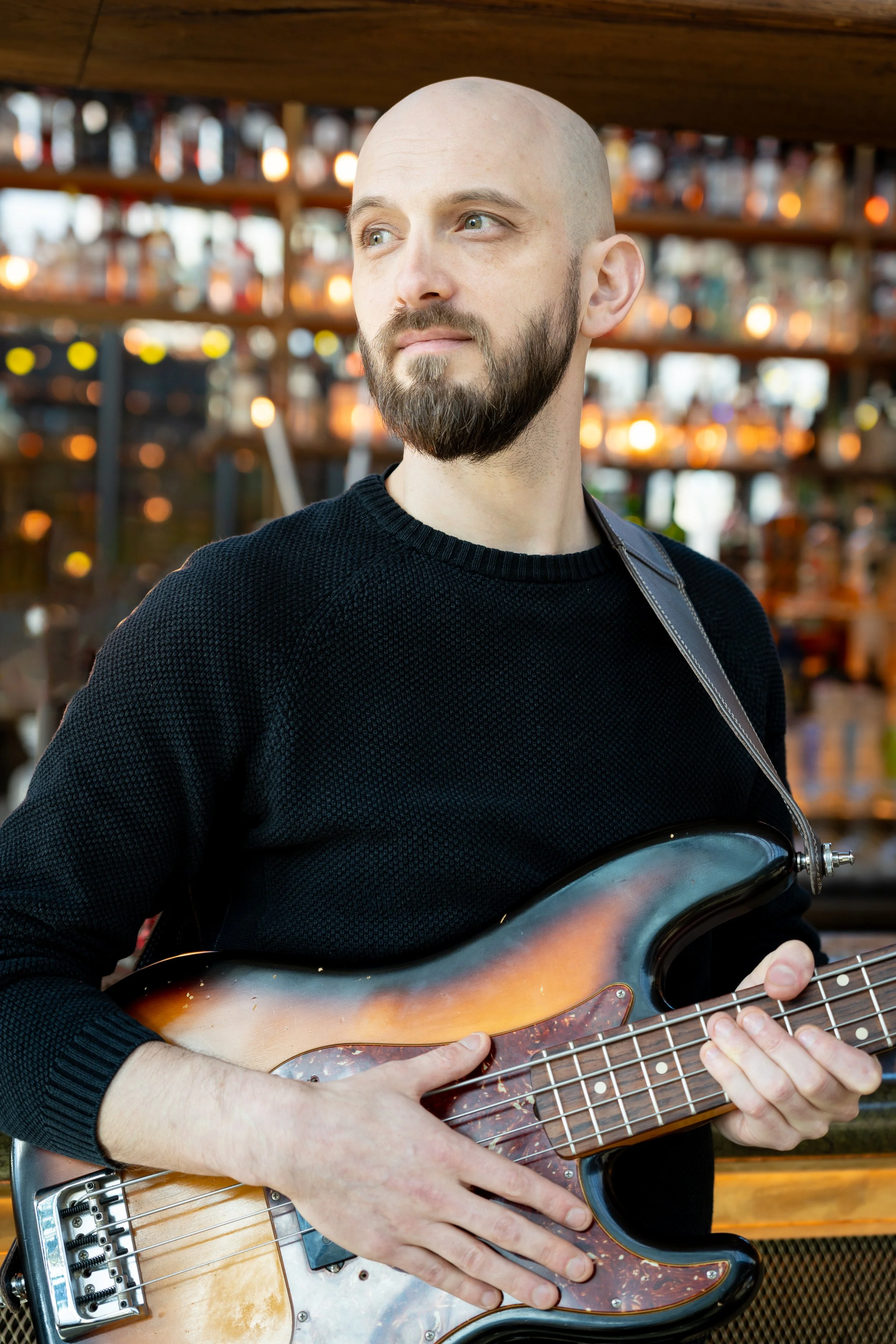Un homme chauve avec barbe qui joue de la guitare électrique dans un lieu avec un décor en arrière-plan.