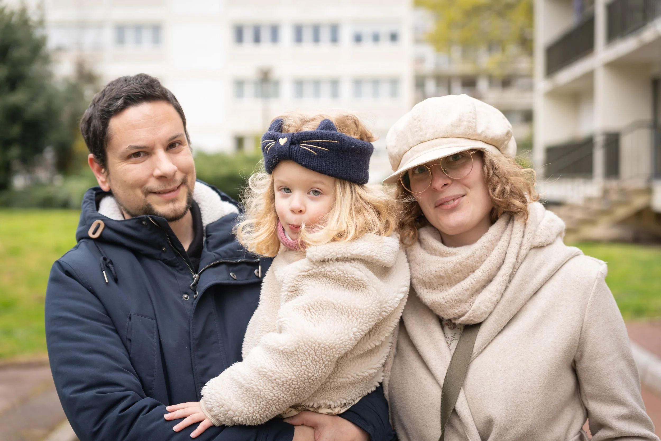 Une famille de trois personnes posant à l'extérieur, un homme, une femme et une petite fille, tous portant des vêtements chauds.