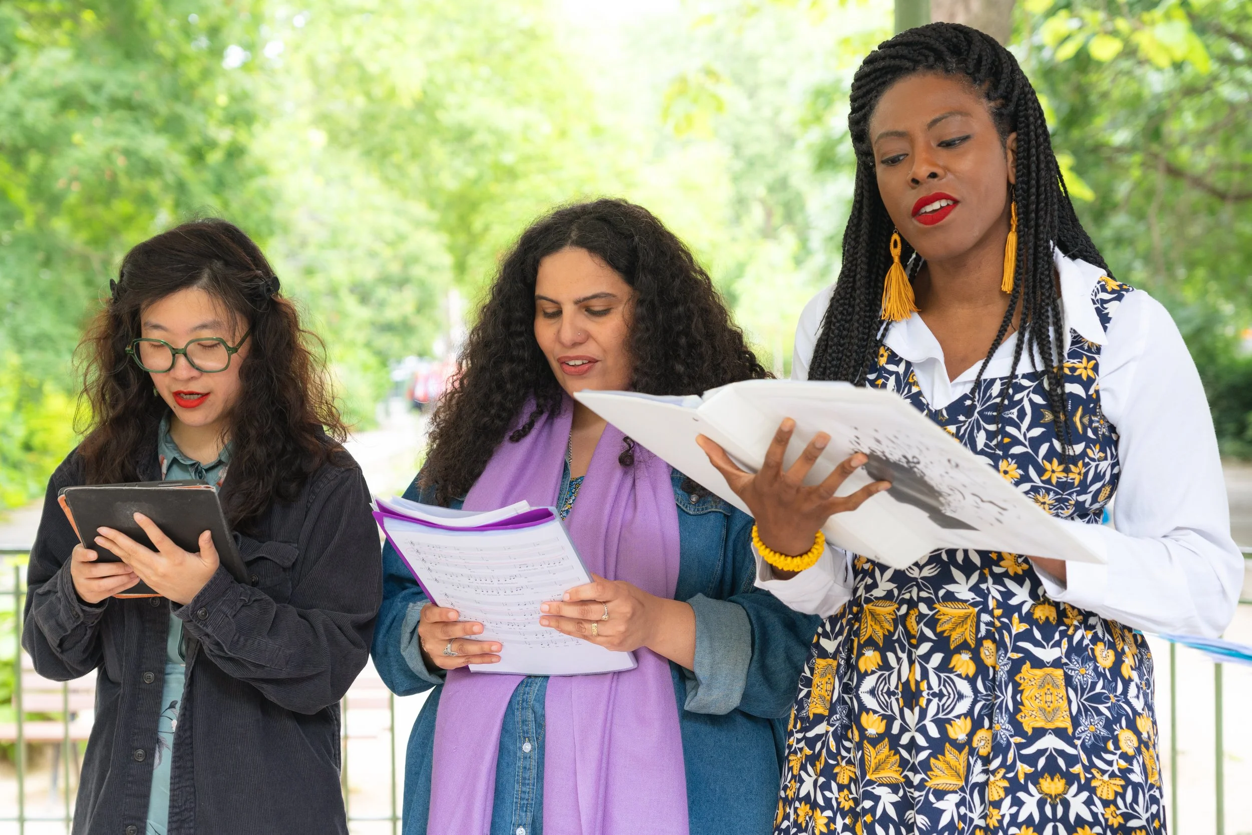 Trois femmes lisant et utilisant un téléphone, dehors dans un parc.