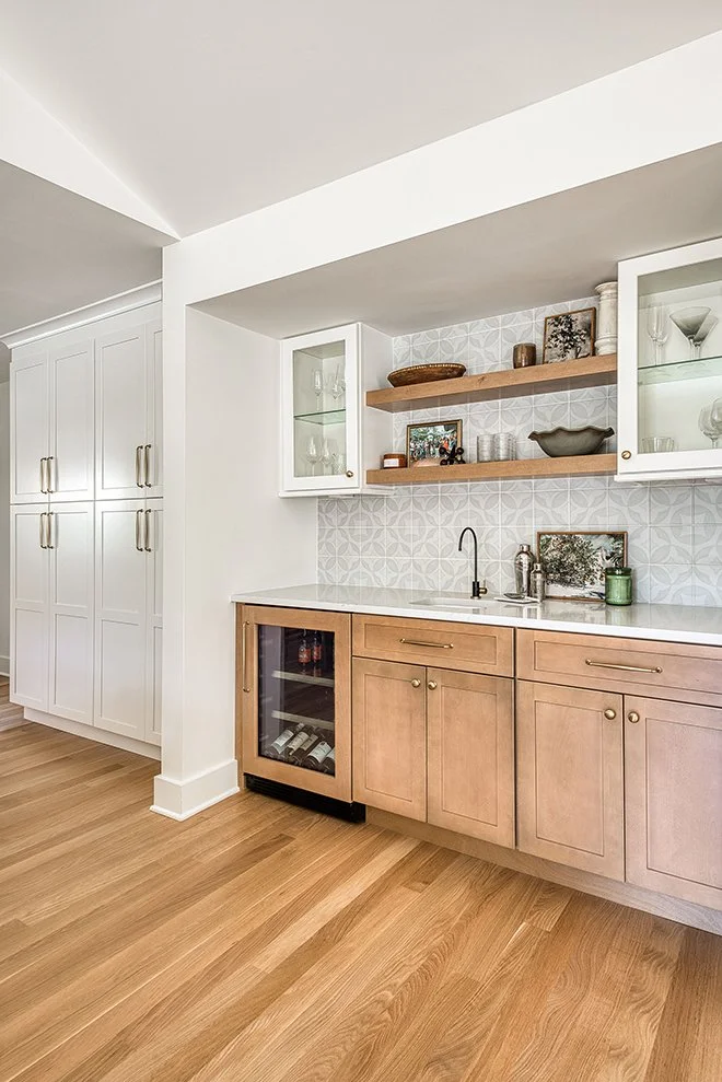 Kitchen with white cabinets, light wood lower cabinets, open shelves, and a wine fridge, with a patterned tile backsplash and a wooden floor.