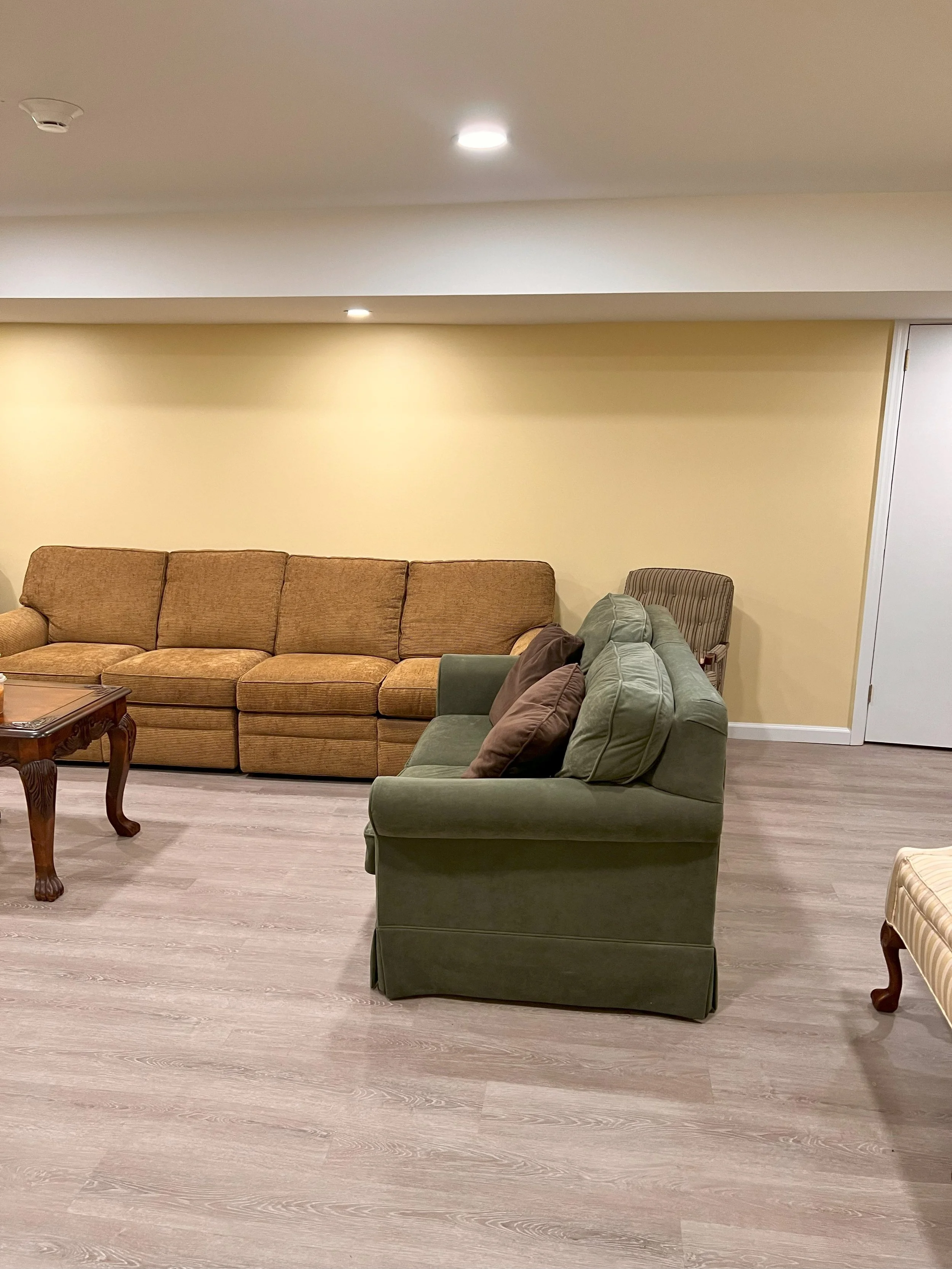 Living room with yellow wall, beige and green couches, wooden coffee table, and hardwood flooring.