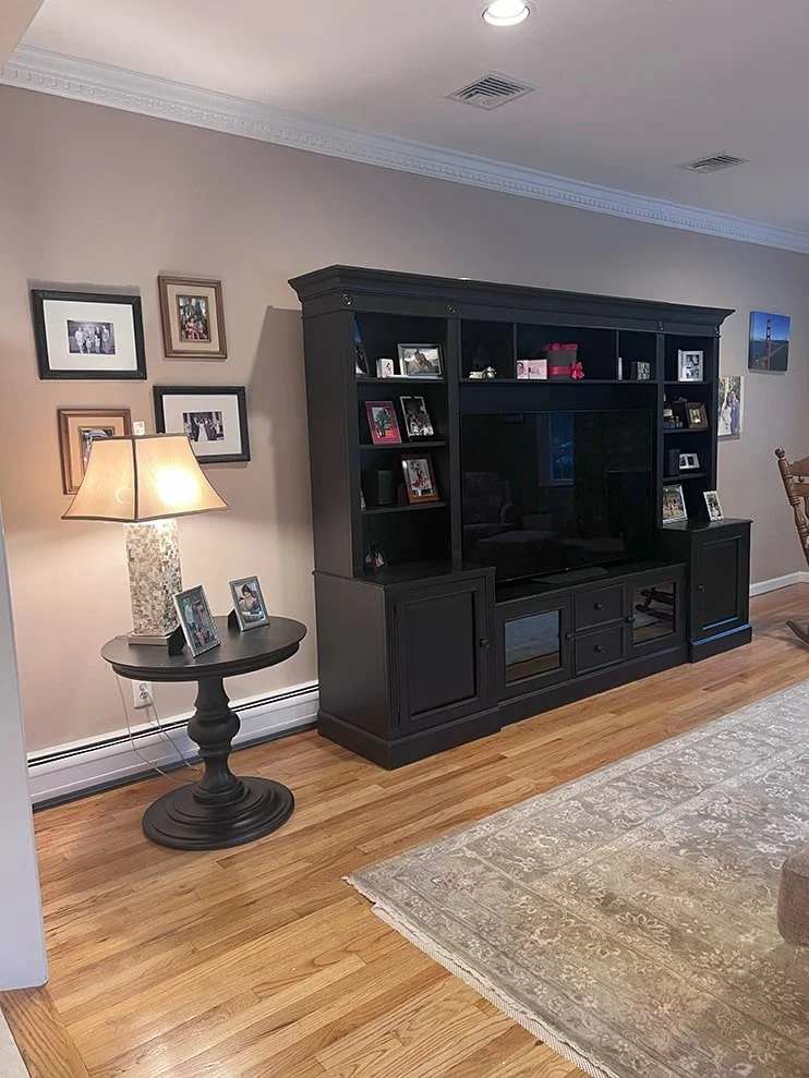 Living room with a black entertainment center, a side table with a lamp and framed photos, and a beige patterned rug on hardwood floor.