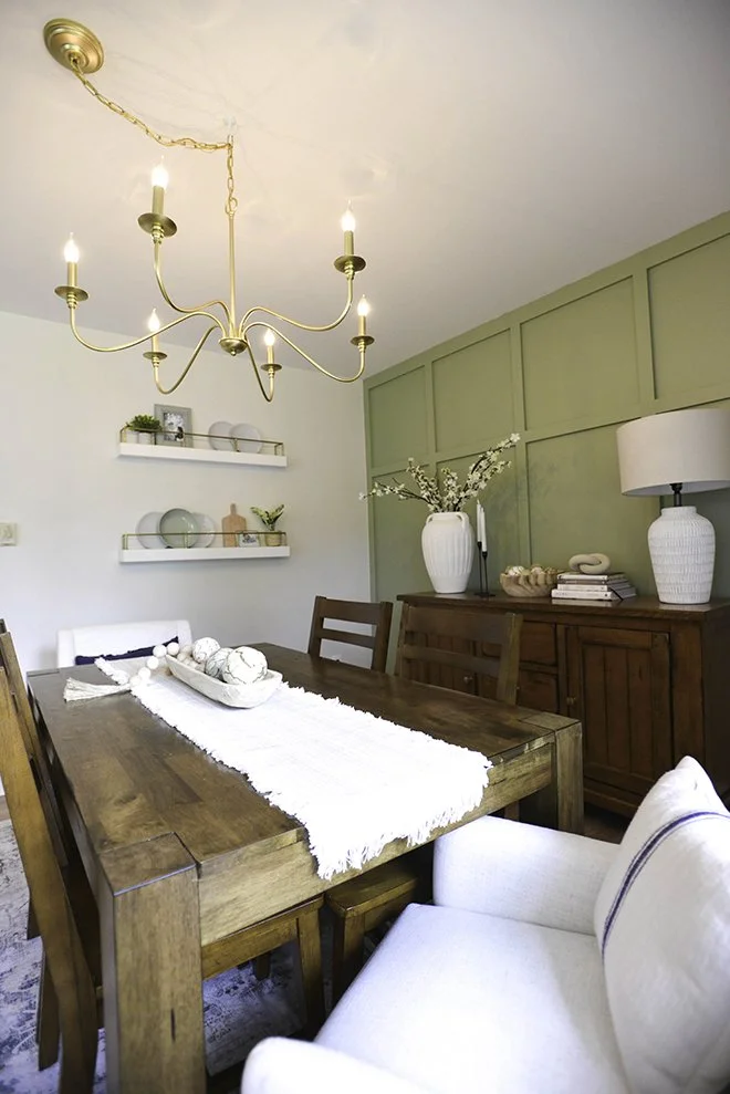A dining room with a wooden table, white and navy chairs, a chandelier, and decorative vases and shelves on the walls.