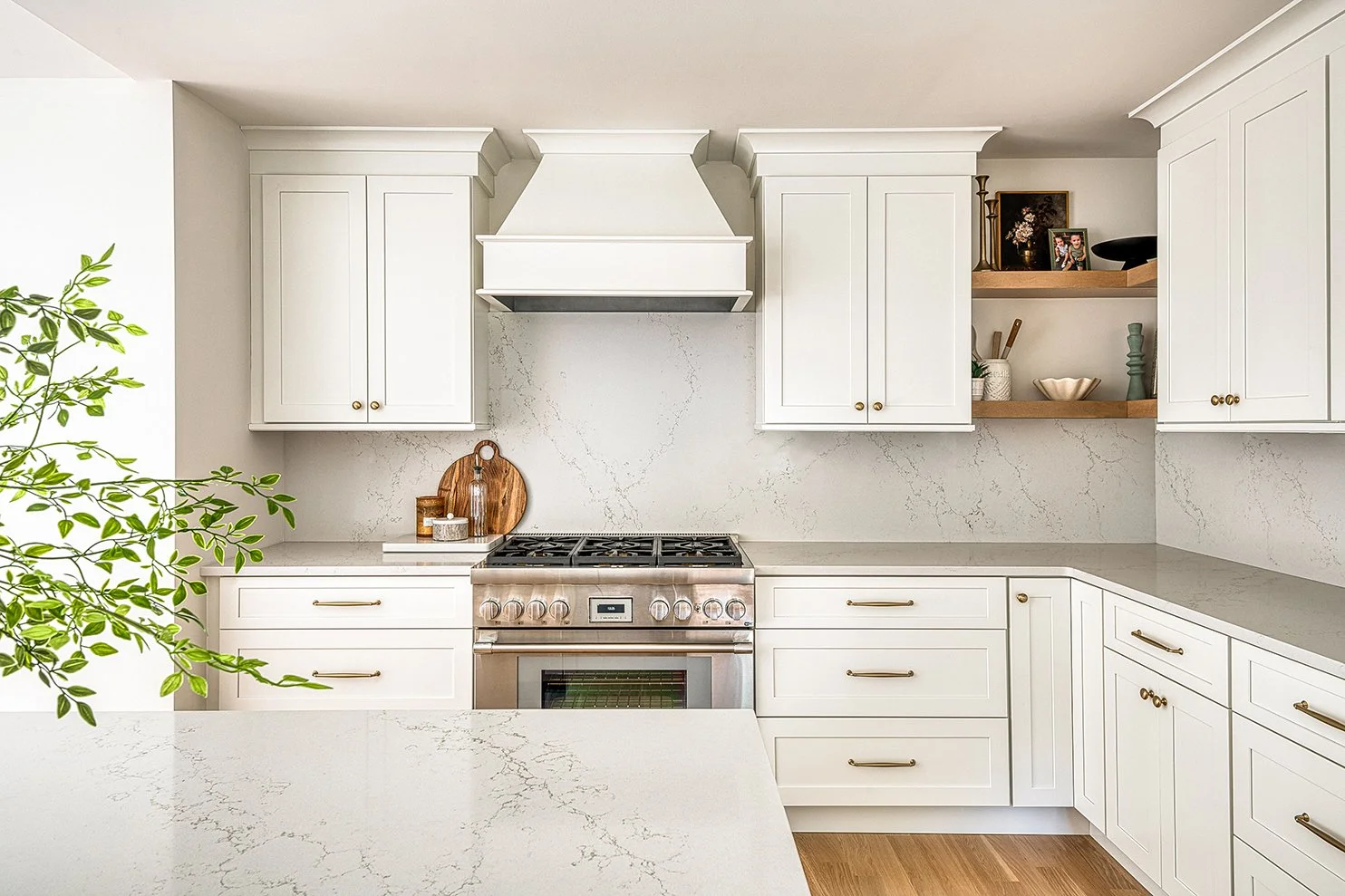 Modern kitchen with white cabinets, marble countertops, and stainless steel stove, decorated with wooden accents and small decorative items.