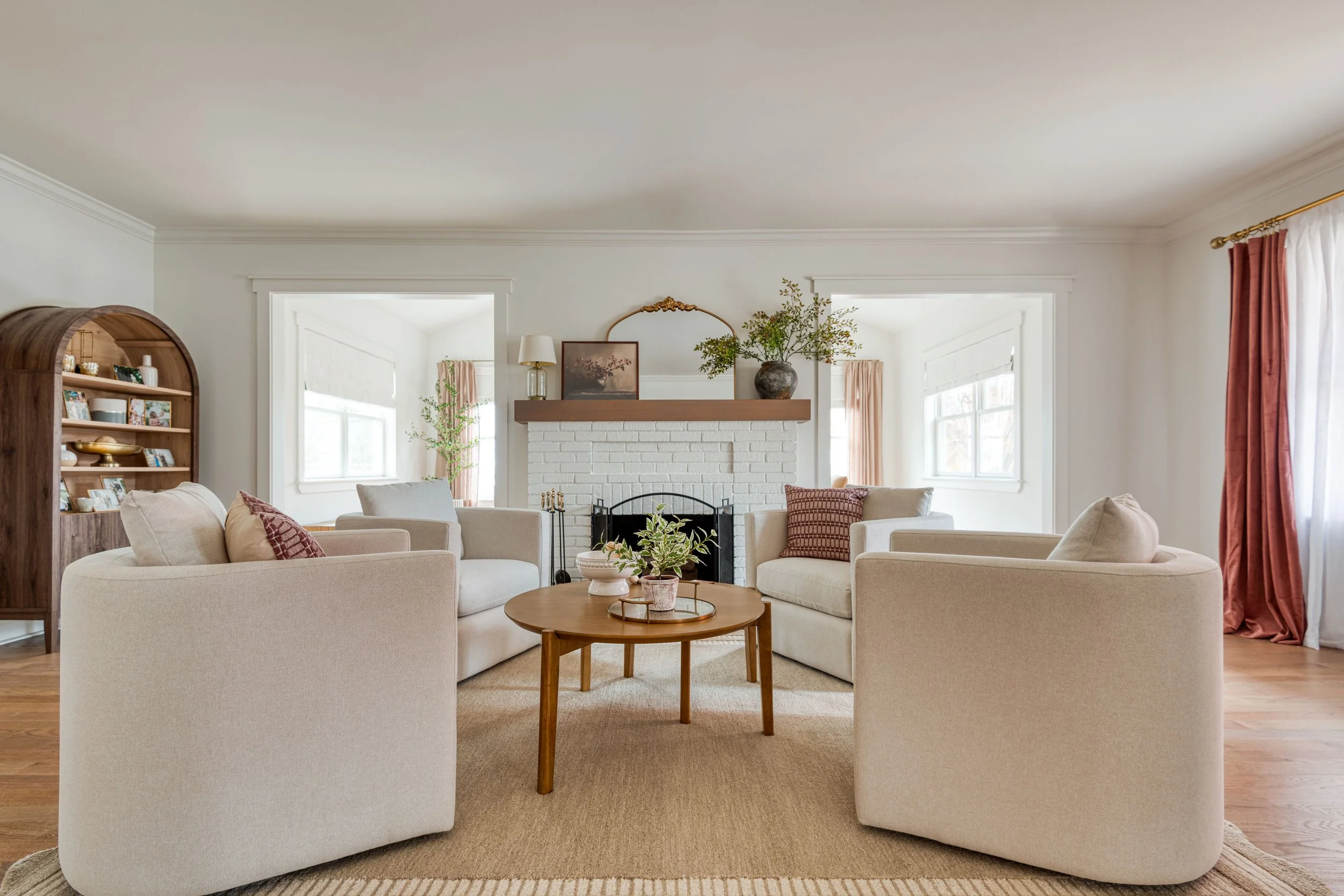 Living room with a white brick fireplace, beige sofas, wooden coffee table, and natural light from multiple windows.