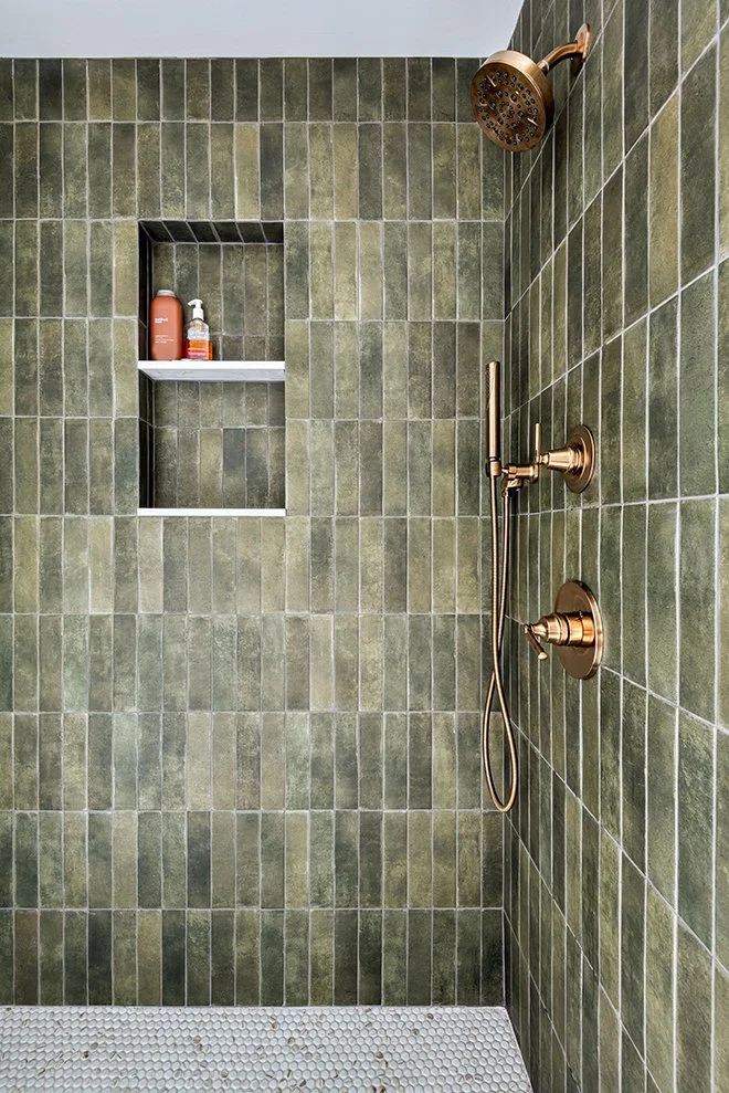 A modern shower with green tile walls, a built-in niche with shampoo and body wash bottles, and brass shower fixtures including a rain showerhead and handheld shower.