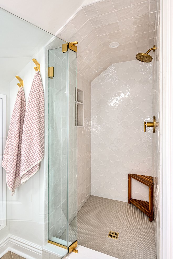 Modern bathroom with a glass shower enclosure, gold fixtures, and two pink checkered towels on gold hooks.