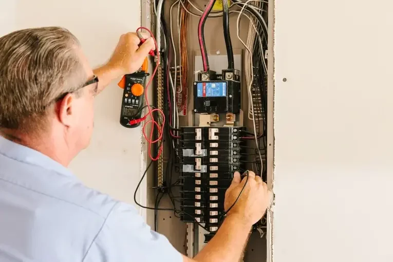 A man inspecting an electrical panel with a multimeter in hand.