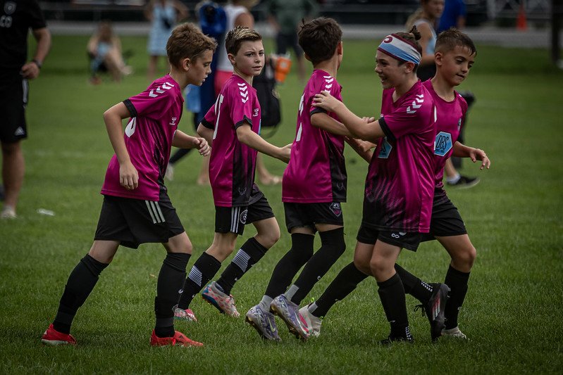 Group of young children in pink soccer jerseys celebrating on a green field.