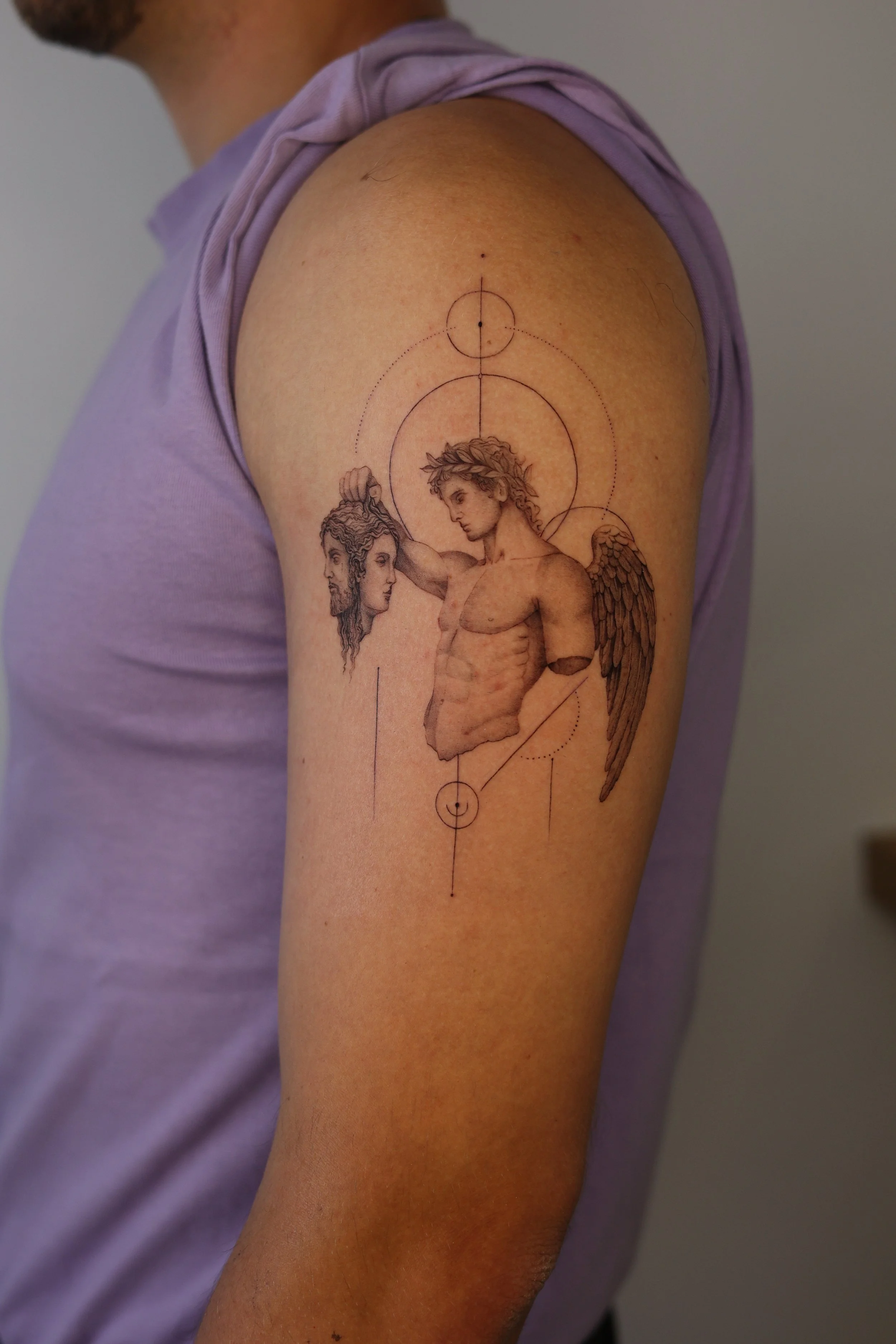 A tattoo featuring a detailed illustration of a winged angel with laurel wreath holding head, crossed by geometric lines and circles in micro realism style done by tattoo artist in Vienna.