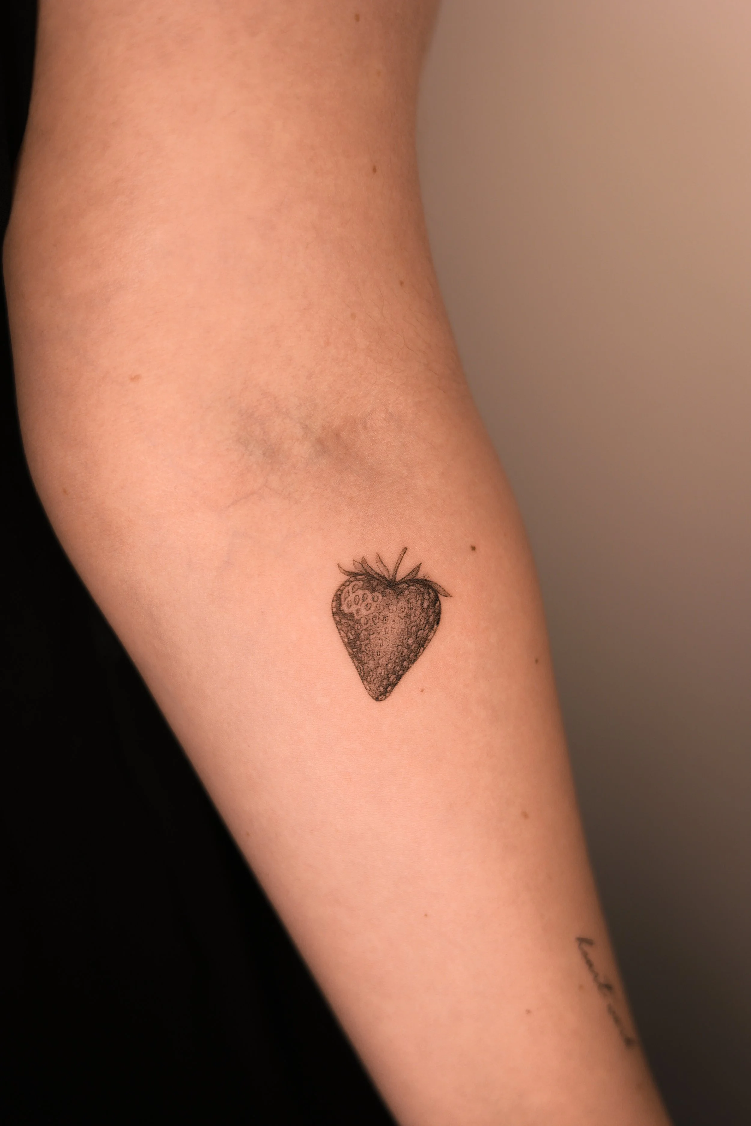 Delicate tattoo of a strawberry in micro realism done by tattoo artist in Vienna.